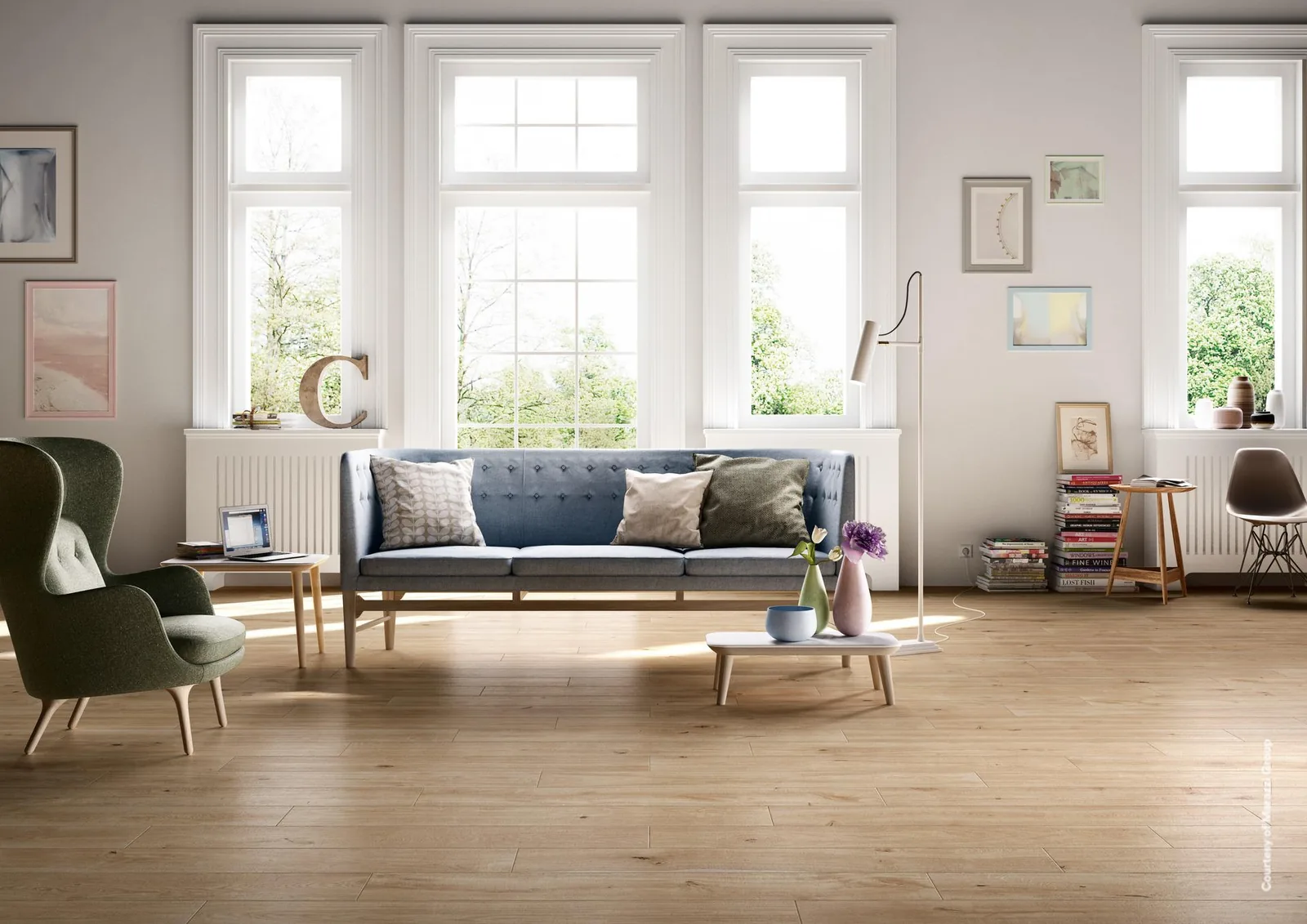 Wohnzimmer mit blauem Sofa, grünem Sessel und hohen Sprossenfenstern, Boden aus honigfarbenen Holzoptik-Dielen.