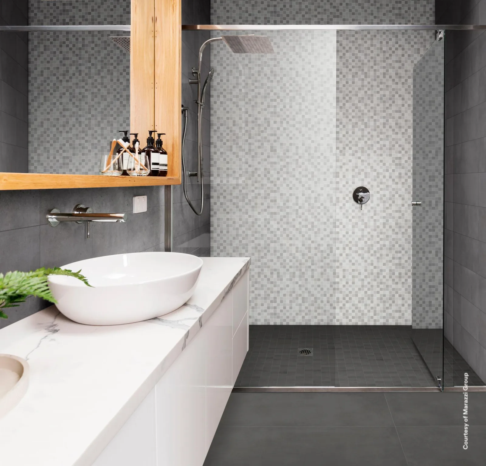 Bad mit Aufsatzwaschbecken, Holzregal und offener Dusche vor grauer Wand mit Mosaikstreifen.