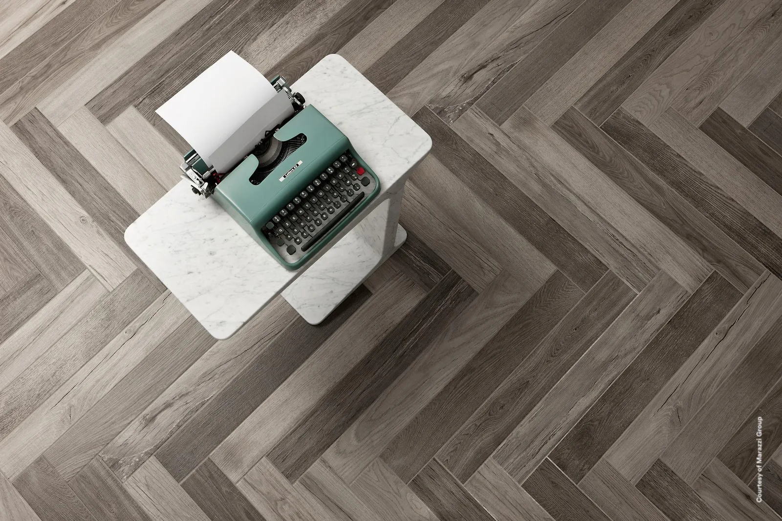 Treverkfusion Grey in Holzoptik im Fischgrätmuster verlegt, von oben mit weißem Beistelltisch und Schreibmaschine