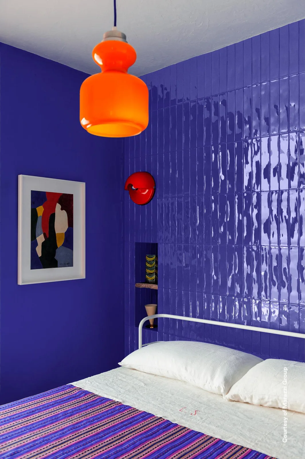 Schlafzimmer mit kobaltblauen, stark glänzenden Riemchen an der Wand hinter dem Bett, orange Pendelleuchte