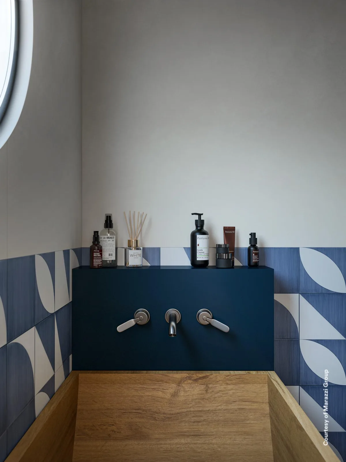 Holzwaschbecken vor blauer Ablage, die Wand ist bis halbe Höhe mit blau-weißen Musterfliesen aus Bögen und Dreiecken belegt.