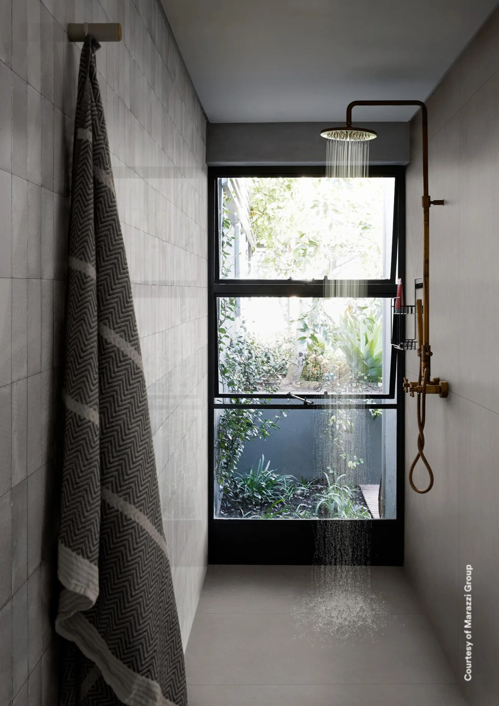 Dusche mit Fenster zum Garten, mittelgraue Betonoptik-Wände, eine davon mit feinem Rillenrelief, Messingarmatur.