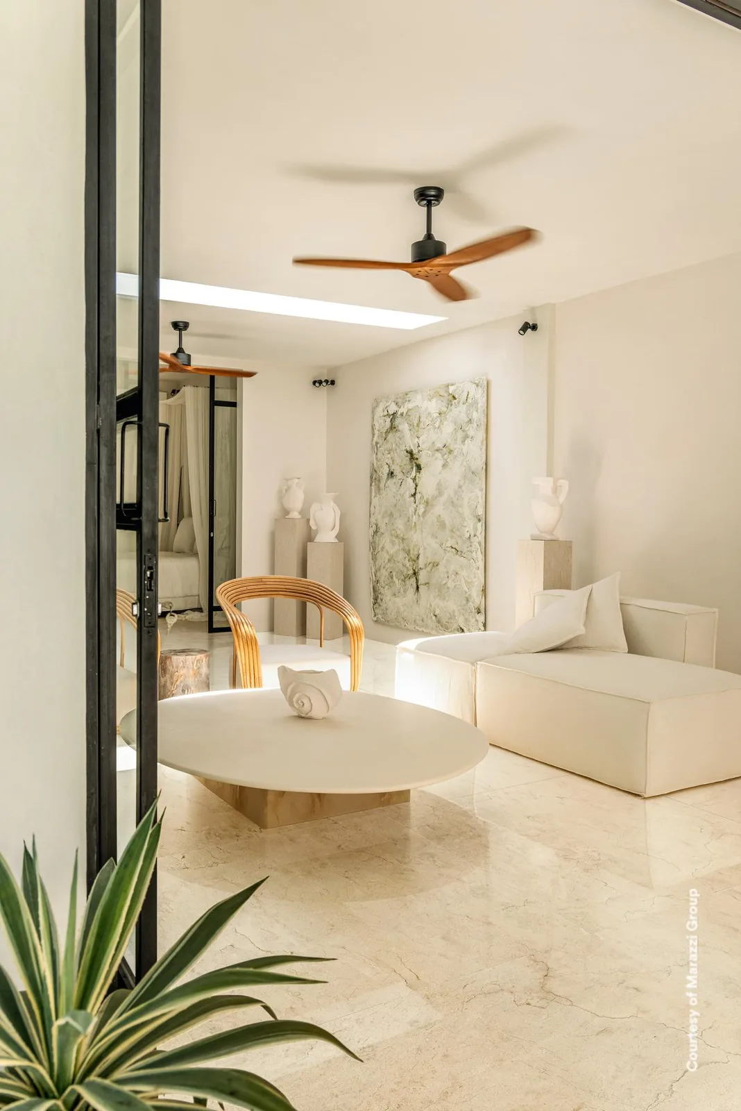 Wohnraum mit rundem Couchtisch, Rattanstuhl und Deckenventilator, Boden in cremefarbener Marmoroptik.