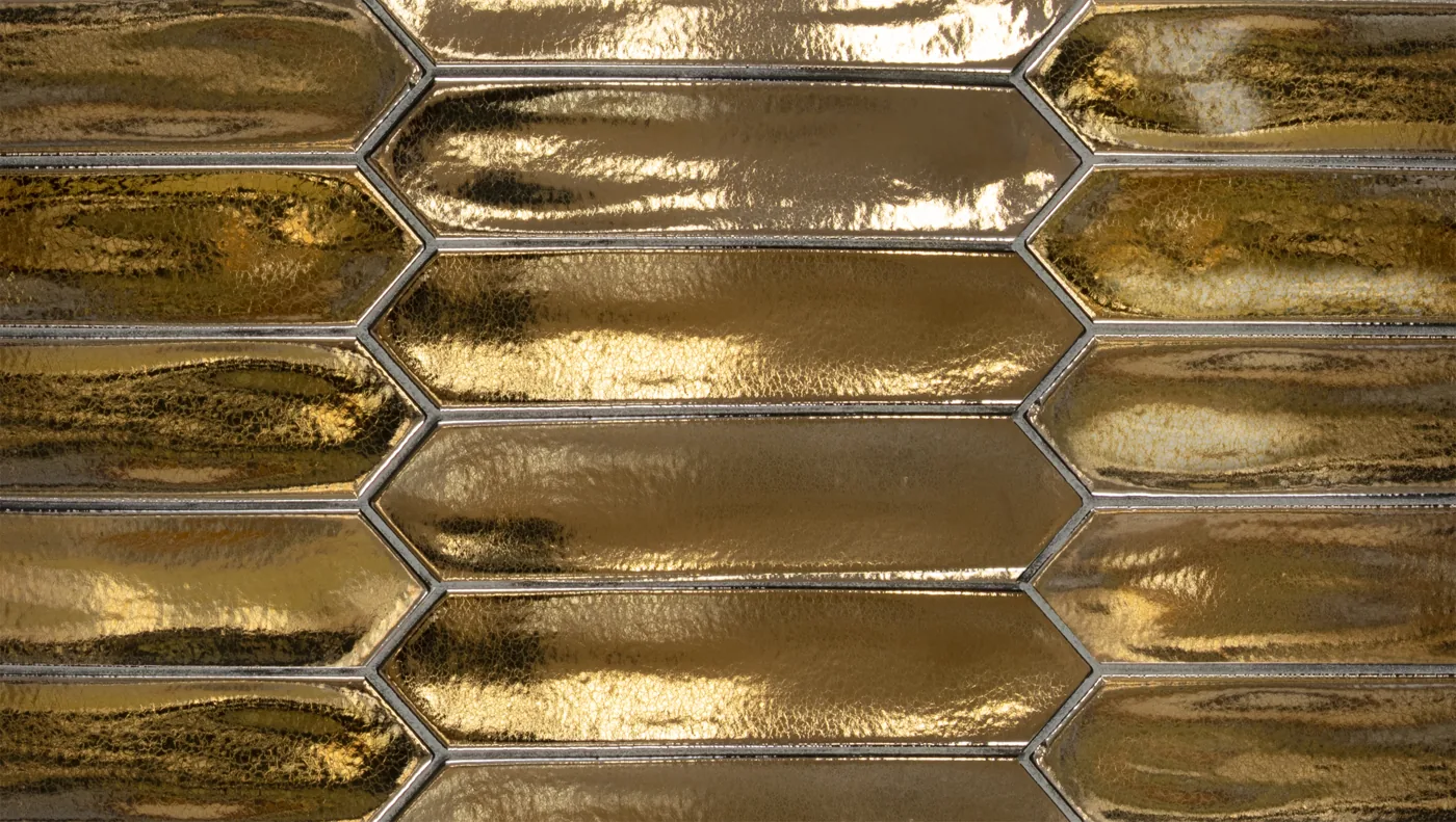 Goldfarbene, spitz zulaufende Wandfliese 5×25 cm, glänzend metallisch glasiert mit spiegelnden Reflexen.
