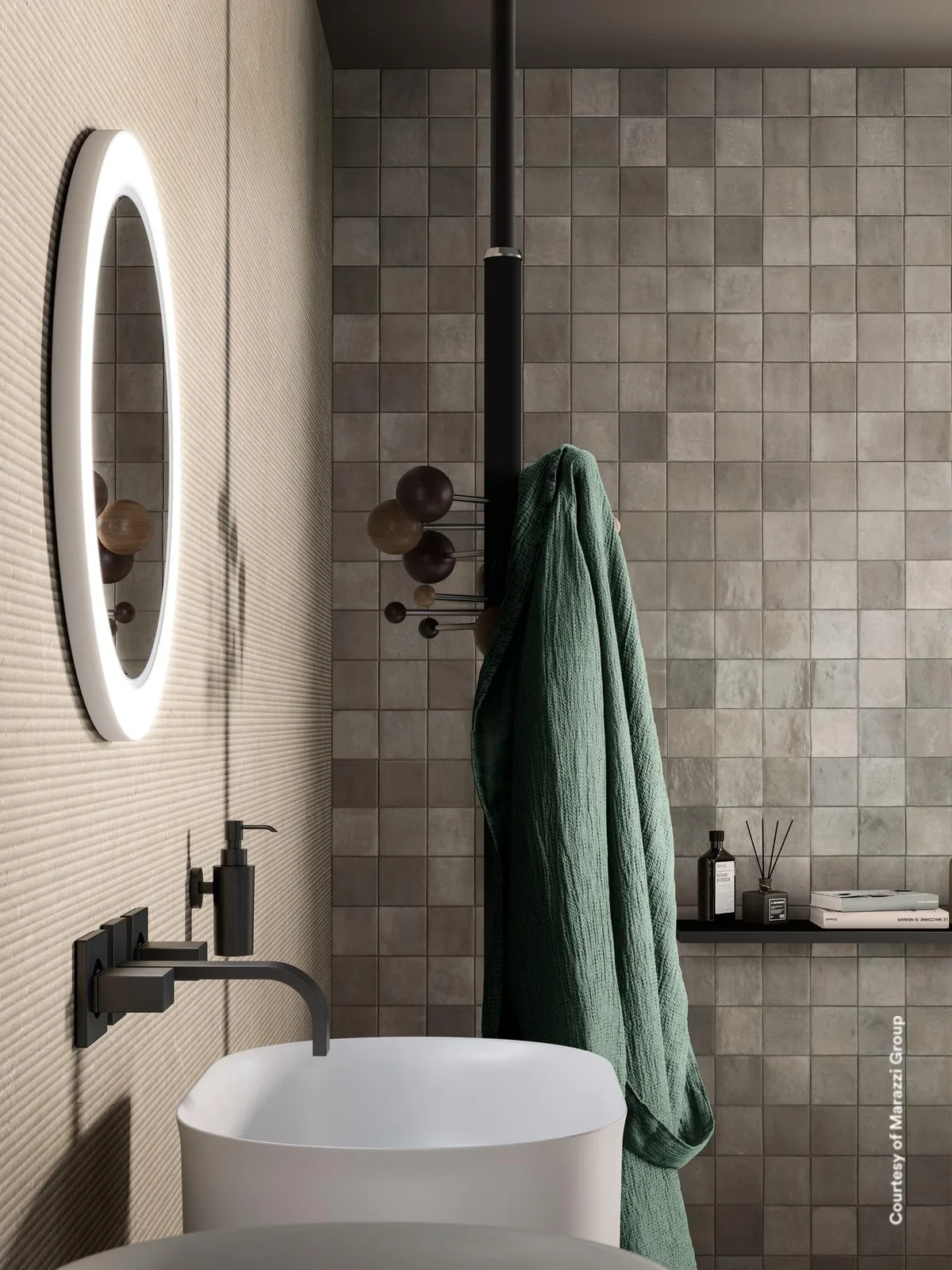 Bad mit Wand aus Marazzi Zellige Argilla 10x10 cm in warmem Grau hinter dem Waschbecken, runder Leuchtspiegel