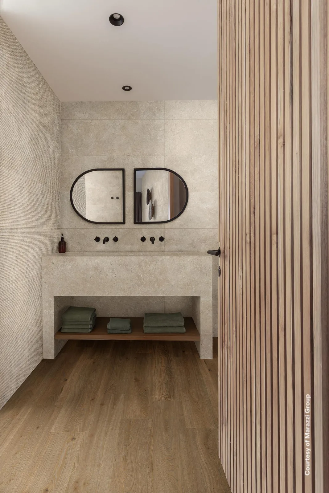 Badezimmer mit sandbeiger Wand in Steinoptik, links mit Rillenrelief, dazu gemauerter Waschtisch und ein Holzboden.