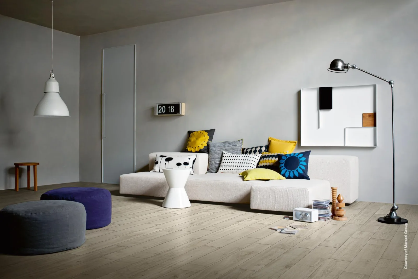 Helles Wohnzimmer mit sehr hellem Dielenboden in Holzoptik, weißem Sofa, blauen Sitzpoufs und einer Stehlampe.