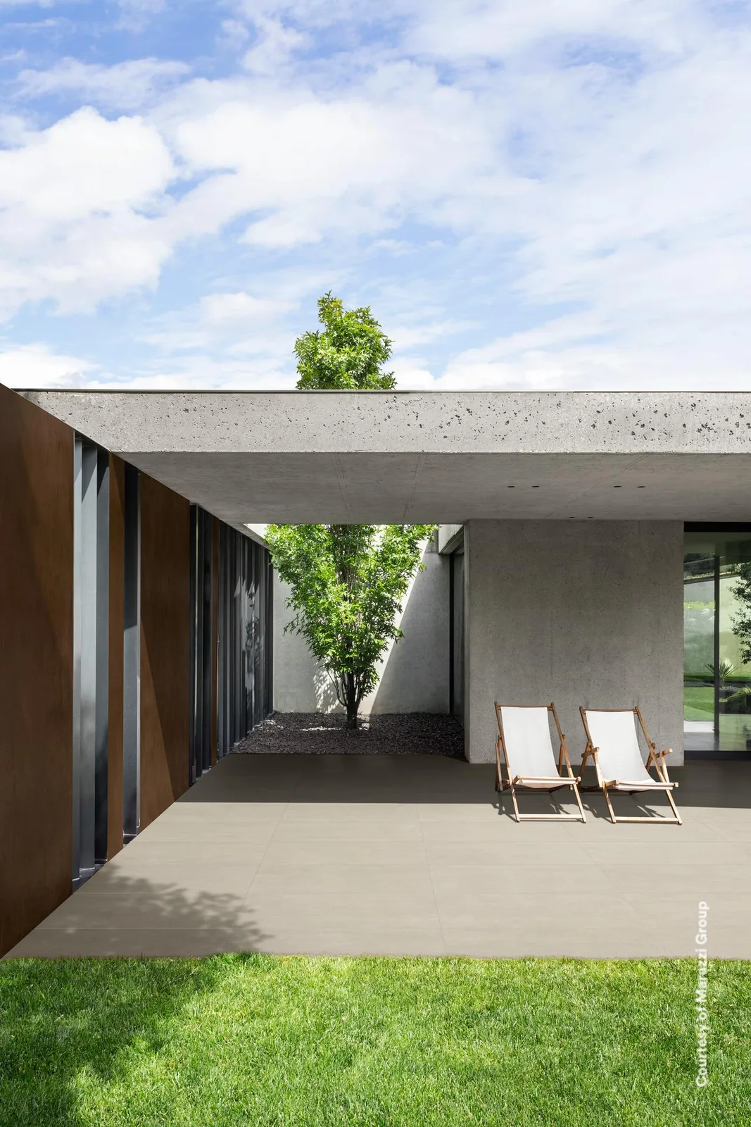 Überdachte Terrasse mit zwei Liegestühlen am Rasen, Boden aus sandbeigen Terrassenplatten 60x120 cm in Betonoptik.