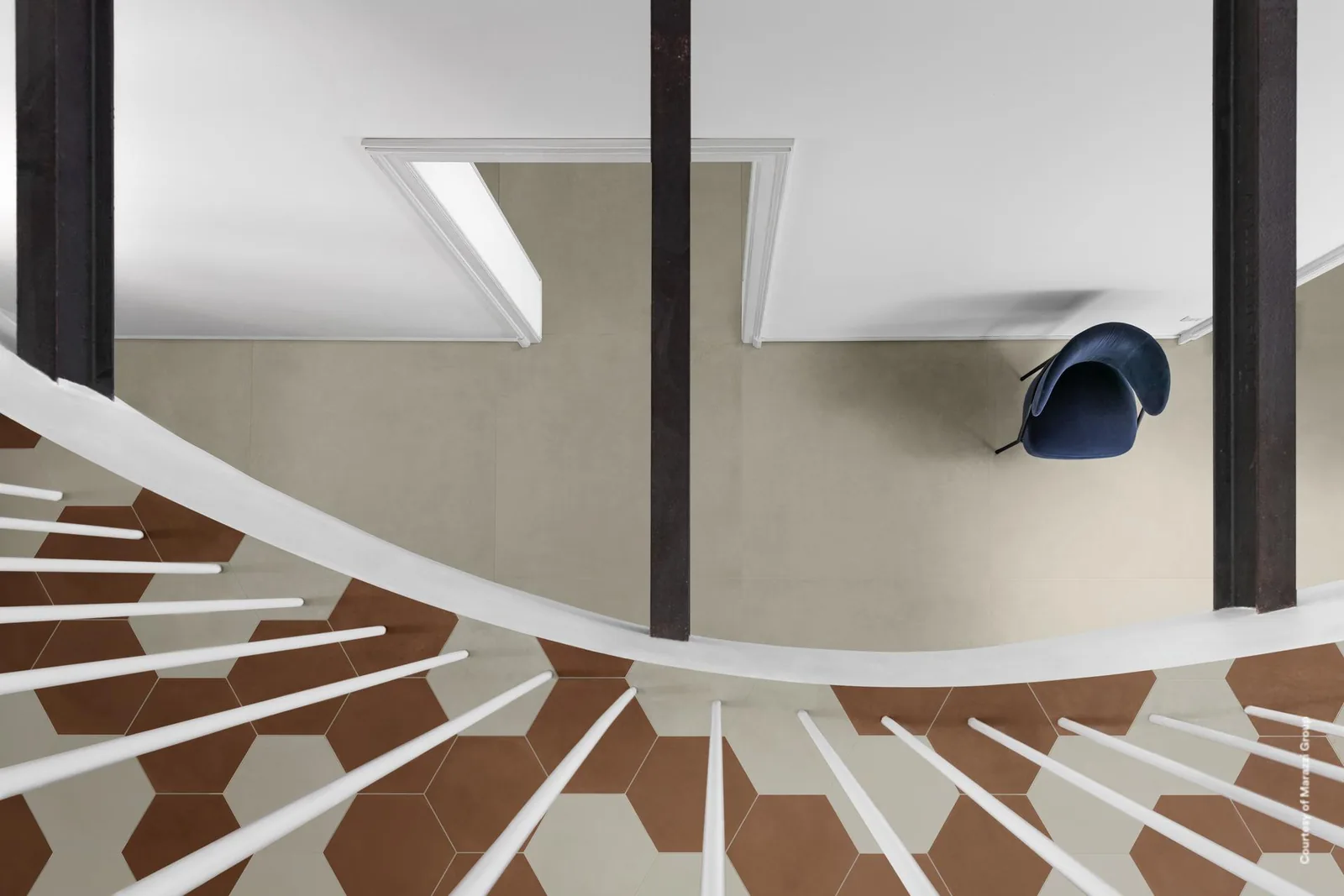 Blick von oben in ein Treppenhaus: hellbeiger Boden in Betonoptik neben braun-weißen Sechseckfliesen und weißem Geländer.
