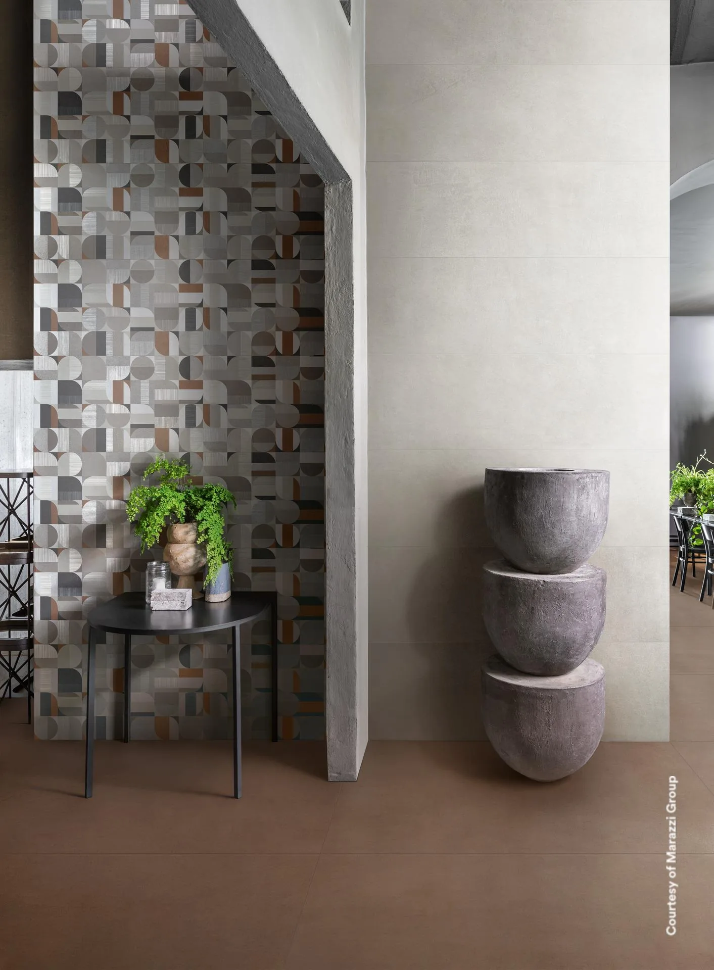 Wohnraum mit geometrisch gemusterter Säule in Grau, Beige und Rostrot, hellbeiger Wand, braunem Boden und Steinschalen