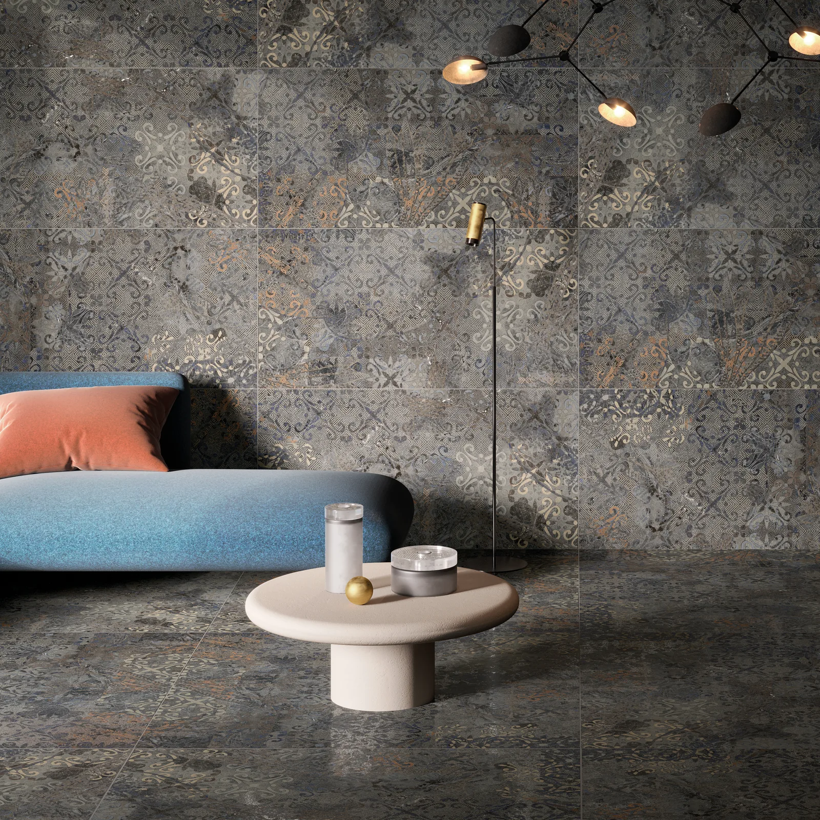 Wohnbereich mit anthrazitfarbenen Dekorfliesen mit Ornament-Patchwork an Boden und Wand, davor ein blaues Sofa.
