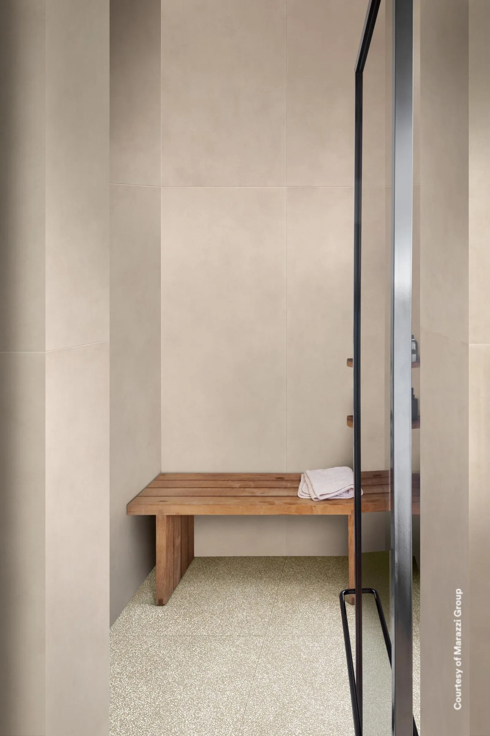 Bodengleiche Dusche mit Holzbank, große beige Wandplatten und heller Terrazzo-Boden mit feinen Splittern.