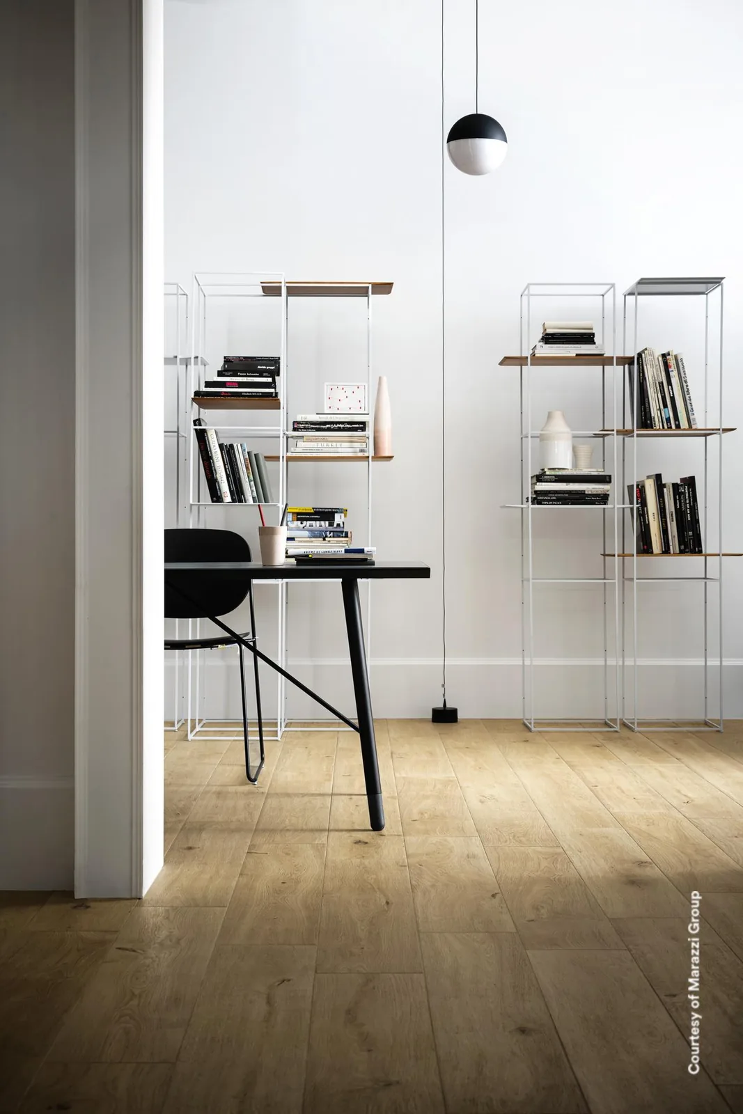 Arbeitsecke mit schwarzem Schreibtisch, Kugelleuchte und Metallregalen auf einem Boden aus naturbeigen Holzoptik-Dielen.