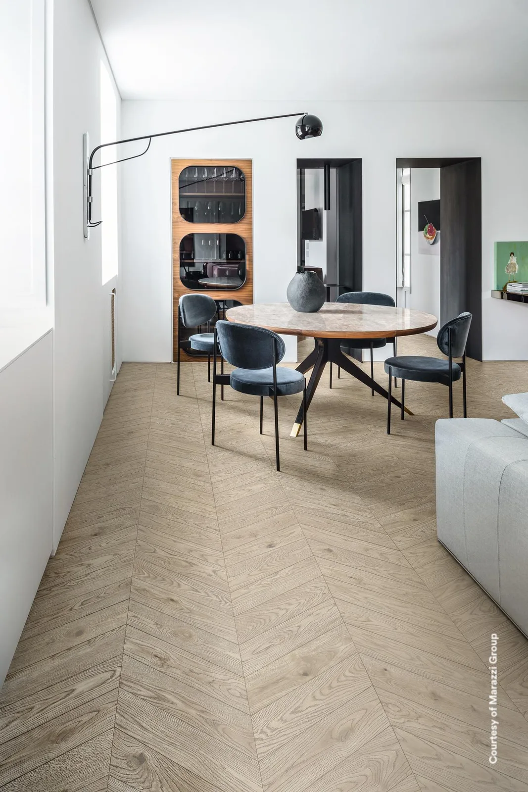 Essbereich mit rundem Tisch und Sofa, Boden in hell sandgrauer Holzoptik im Fischgrätmuster verlegt.