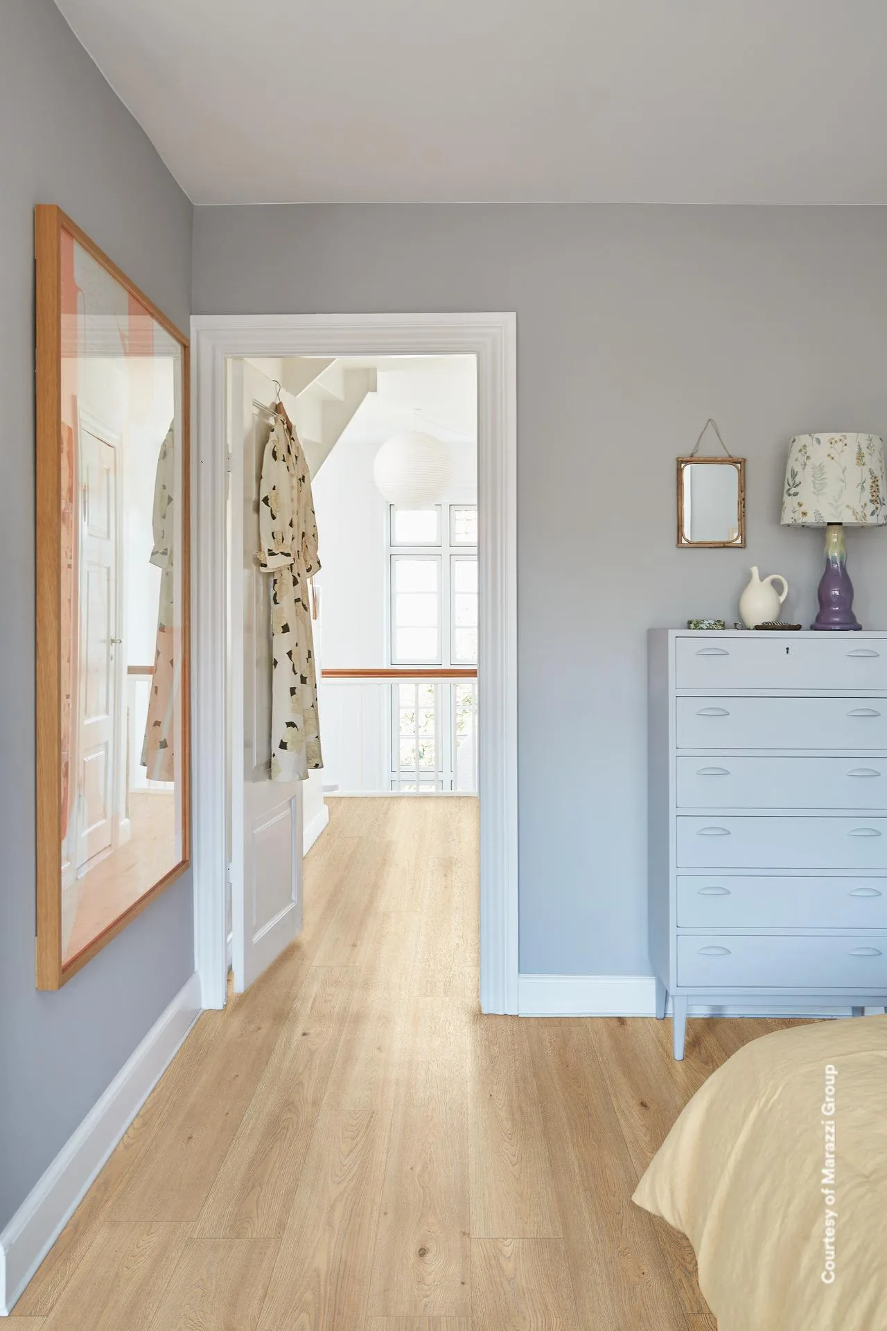 Schlafzimmer mit grauer Wand, hellblauer Kommode und offener Tür zum Flur, heller Holzdielenboden