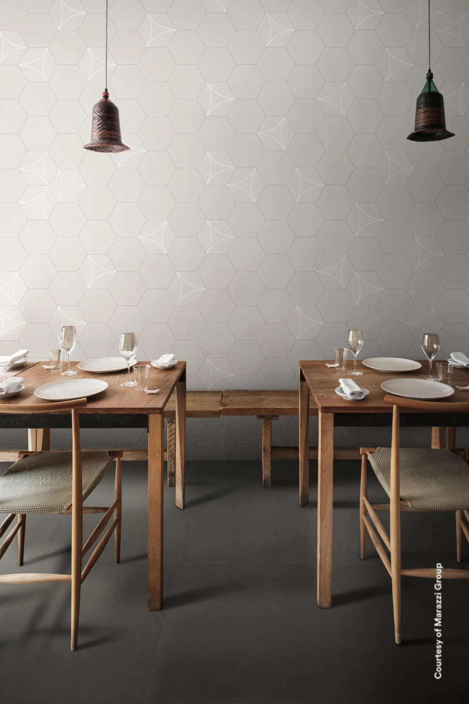 Restaurant mit Holztischen und Pendelleuchten, hellgraue Sechseckwand mit Bogenlinien über anthrazitfarbenem Boden.