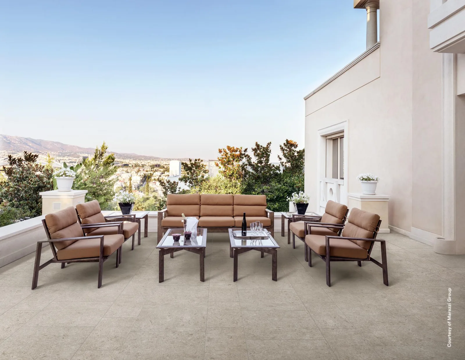 Dachterrasse mit hellem, cremeweißem Steinoptik-Boden, Ledersesseln und Couchtisch, im Hintergrund Hügellandschaft.
