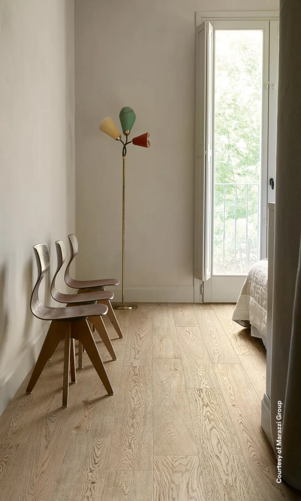 Zimmer mit gestapelten Holzstühlen und Stehlampe an der Balkontür, Boden in hellbeigen Holzoptik-Planken.