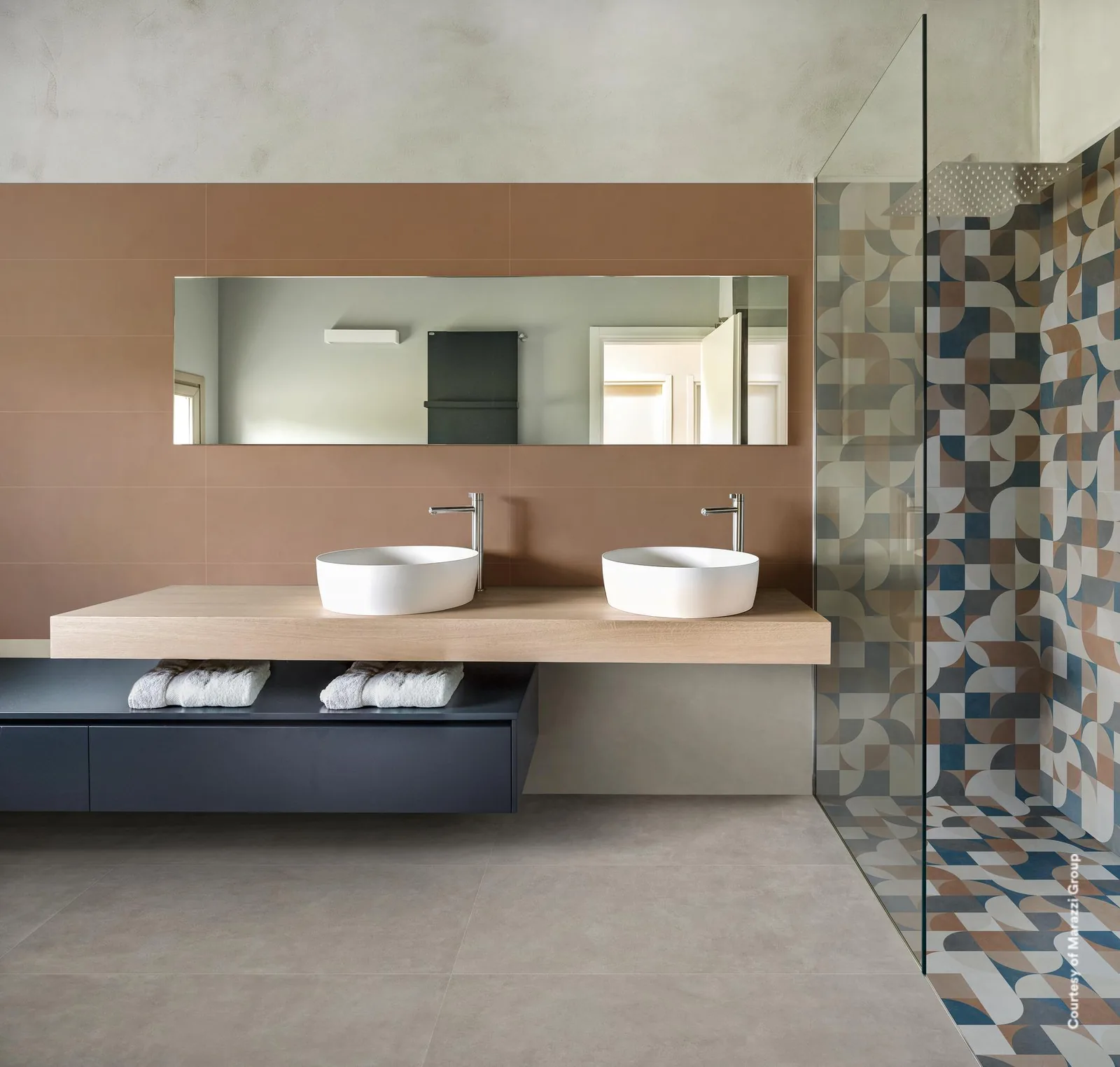 Bad mit terrakottafarbener Wand hinter dem Waschtisch, hellem Betonoptik-Boden und Dusche mit buntem Geometriedekor.