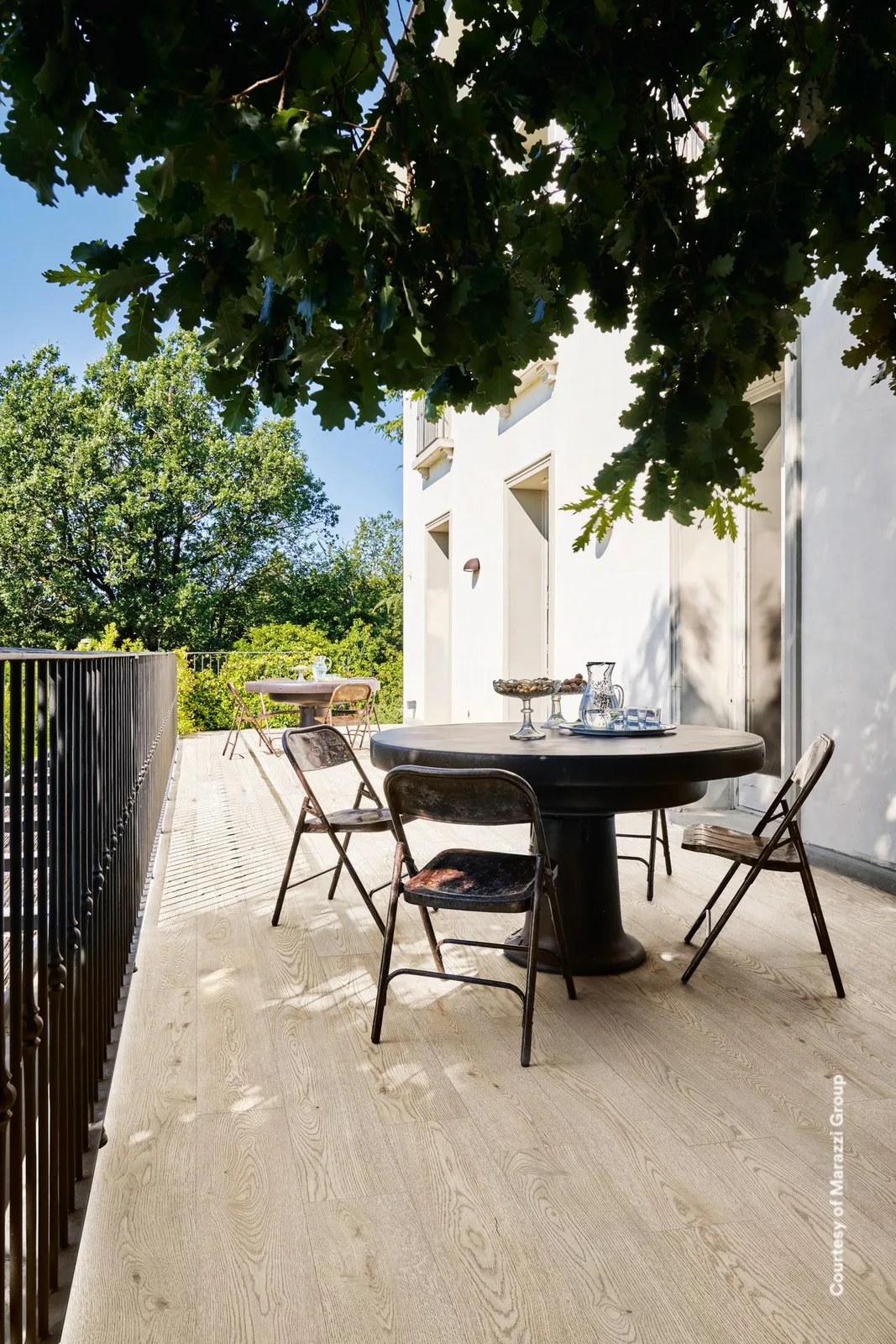 Überdachte Terrasse mit rundem Tisch und Klappstühlen, Boden in hell sandgrauen Holzoptik-Planken verlegt.