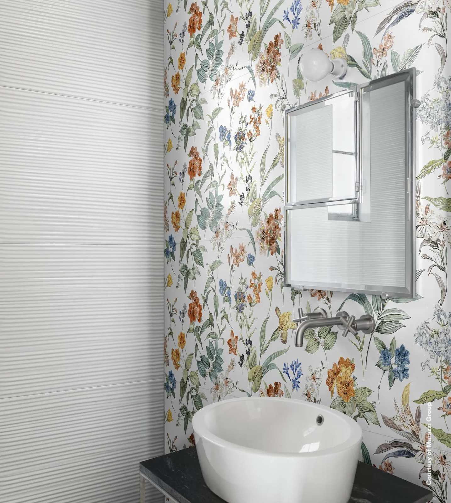 Badezimmer mit Waschtisch und Spiegel vor einer Wand mit bunten Blumen, links daneben weiße Wand mit Rillenstruktur.