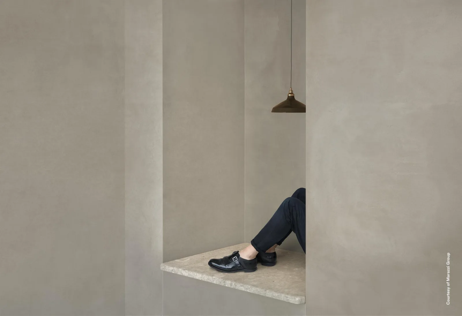 Wandnische mit sitzender Person, Wände und Boden aus großformatigen Platten in warmem, hellem Graubeige.