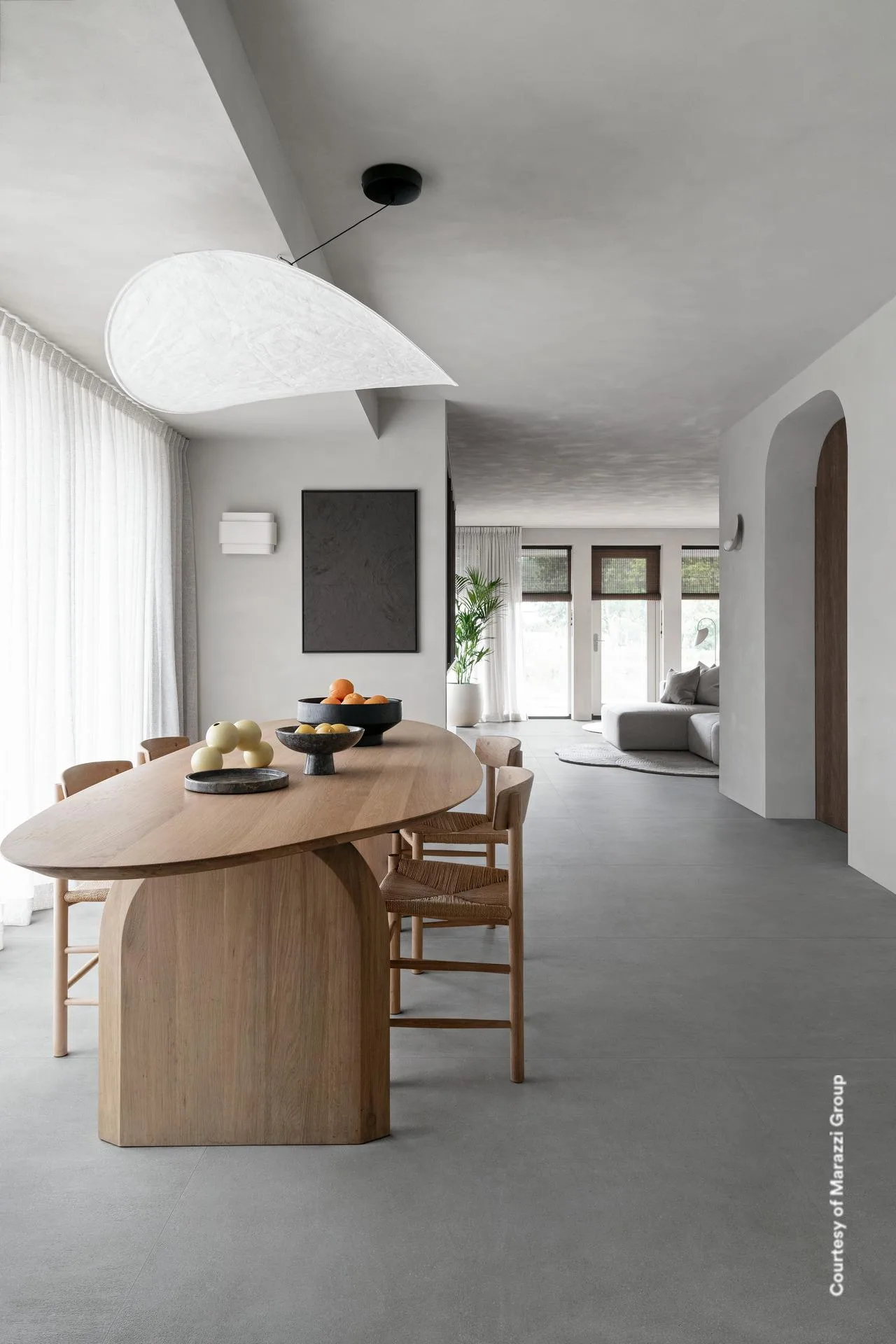 Offener Wohn-Essbereich mit ovalem Holztisch und großer Pendelleuchte auf mittelgrauem Betonoptik-Boden 120x120 cm.