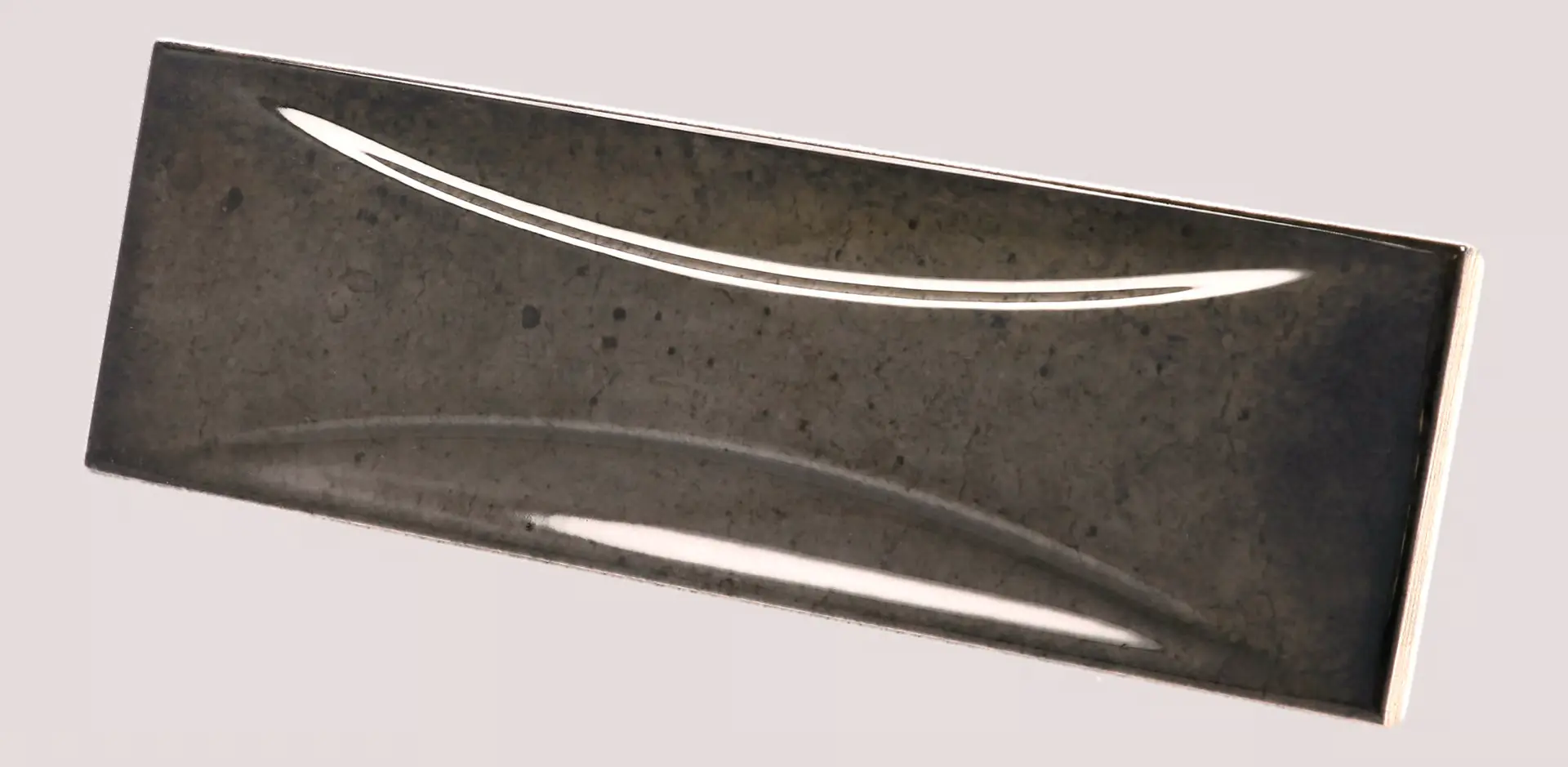 Hanoi Wandfliese in Black Ash Glasur, Format 6,5x20 cm, schräge Studio Aufnahme mit sichtbarem Glasurglanz.