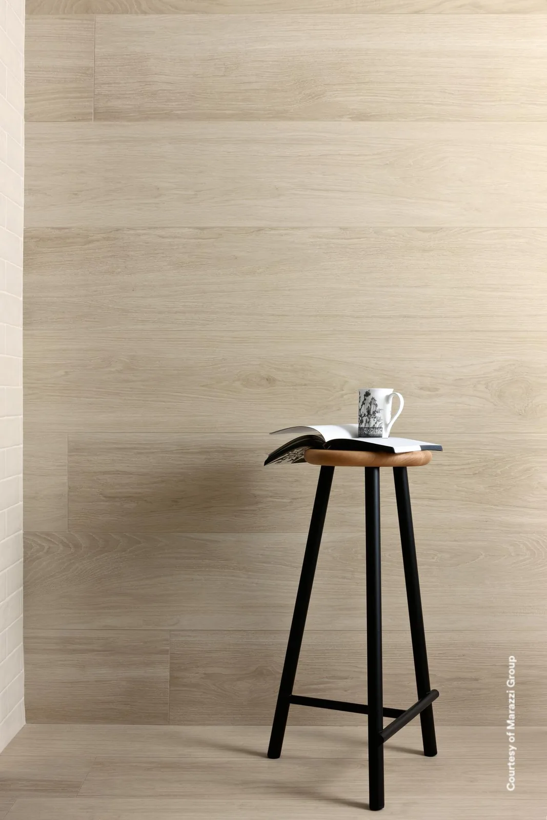 Wand aus hellen, weißlich-beigen Holzoptik-Dielen, davor ein schwarzer Barhocker mit aufgeschlagenem Buch und Tasse.
