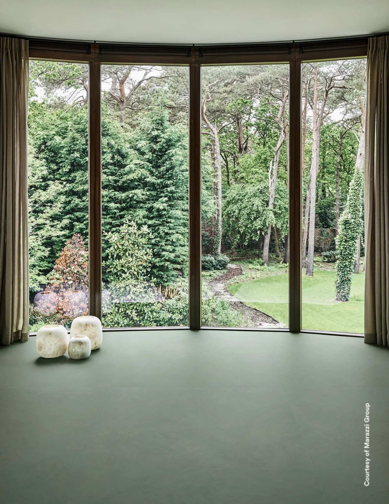 Raum mit dunkelgrünem Bodenbelag und Wänden, geschwungene Fensterfront mit Blick in den Garten