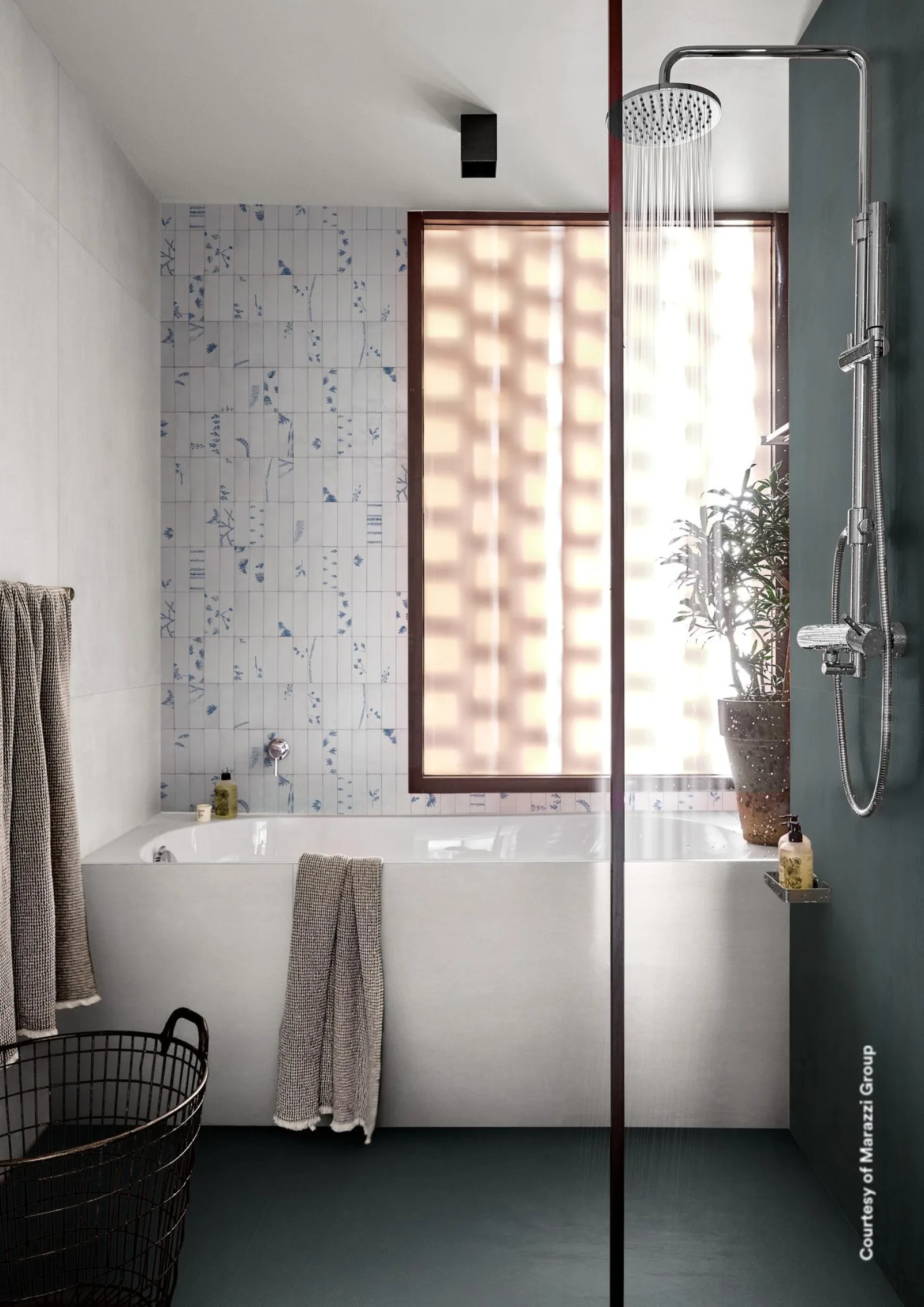 Badezimmer mit blaugrauem Betonoptik-Boden, hellgrauer Wand, Badewanne und blau gemusterter Mosaikwand am Fenster.