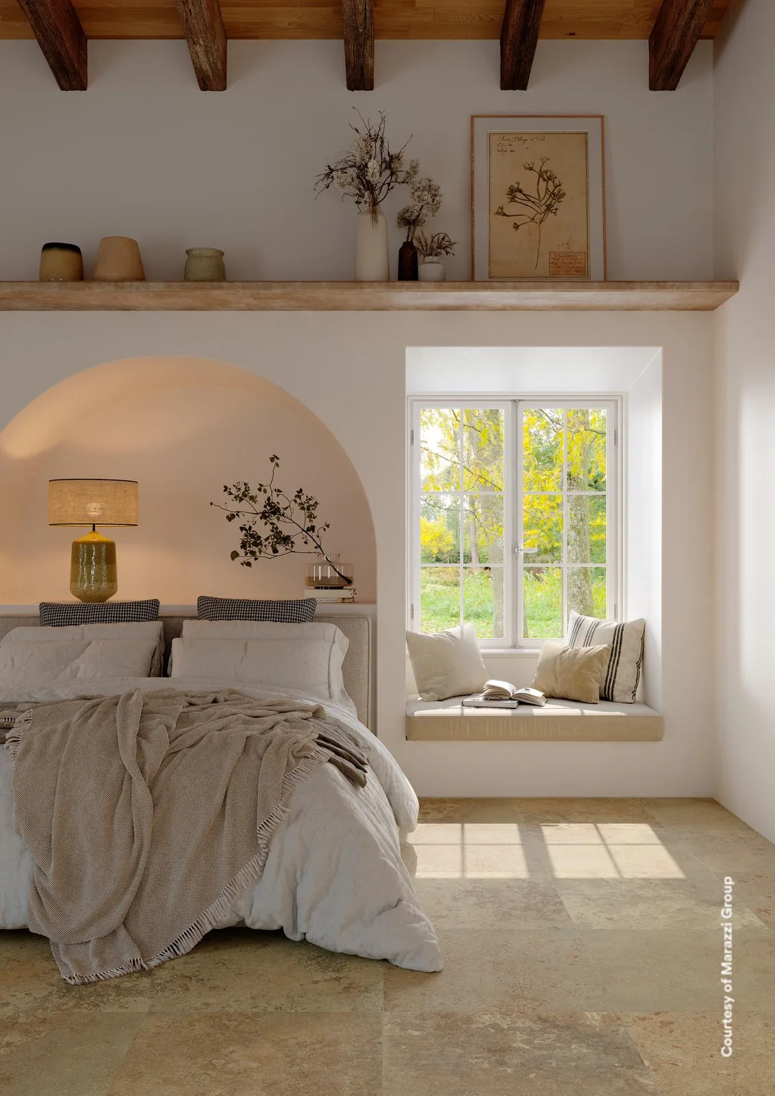 Schlafzimmer mit beigen Steinoptik-Bodenfliesen, Holzbalkendecke, Bogennische mit Leuchte und Fenstersitz