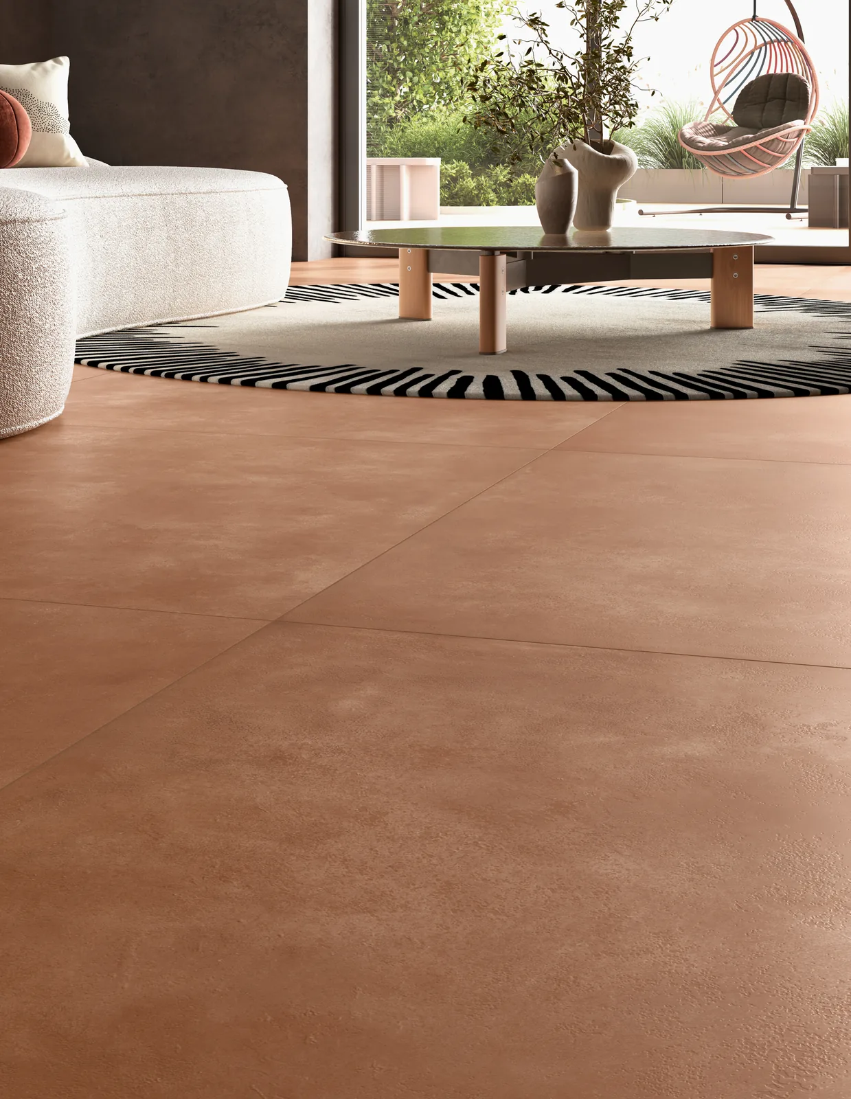 Wohnbereich mit orangebraunem Großformat-Boden, gestreiftem Rundteppich, Couchtisch und Blick in den Garten