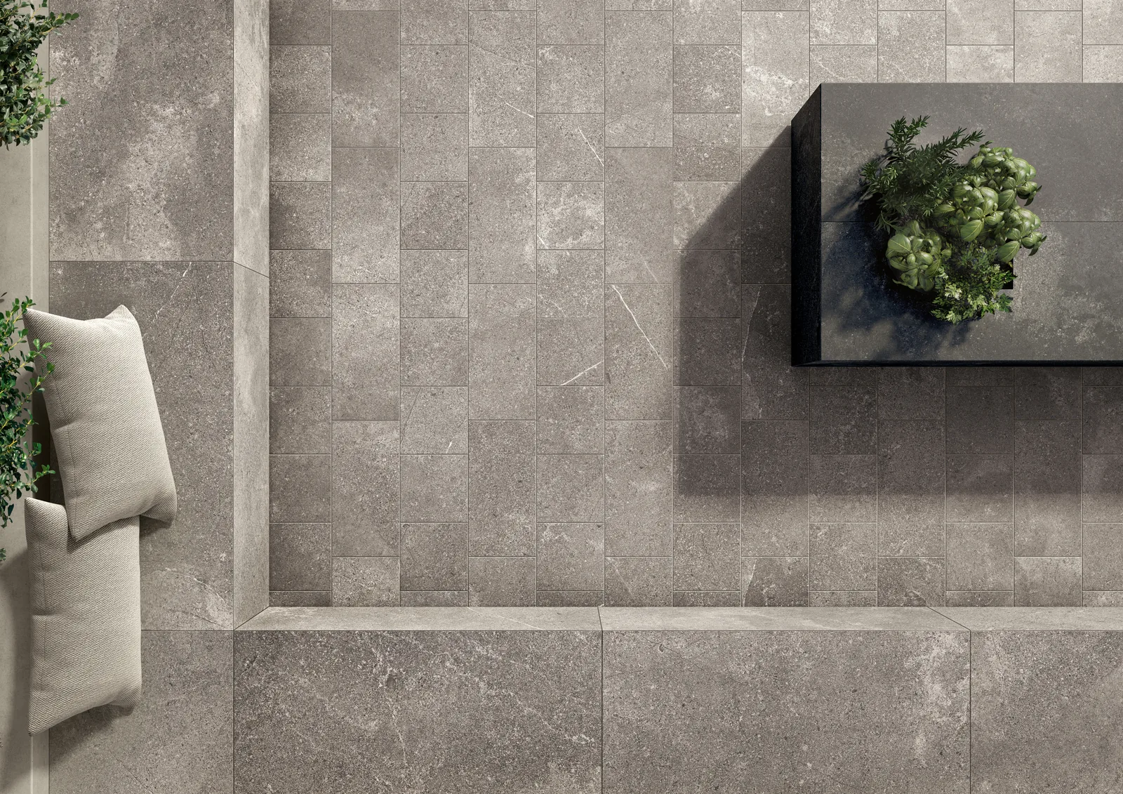 Terrasse von oben mit grauen Steinoptik-Fliesen im Kleinformat, Sitzbank mit Kissen und Pflanzkasten.