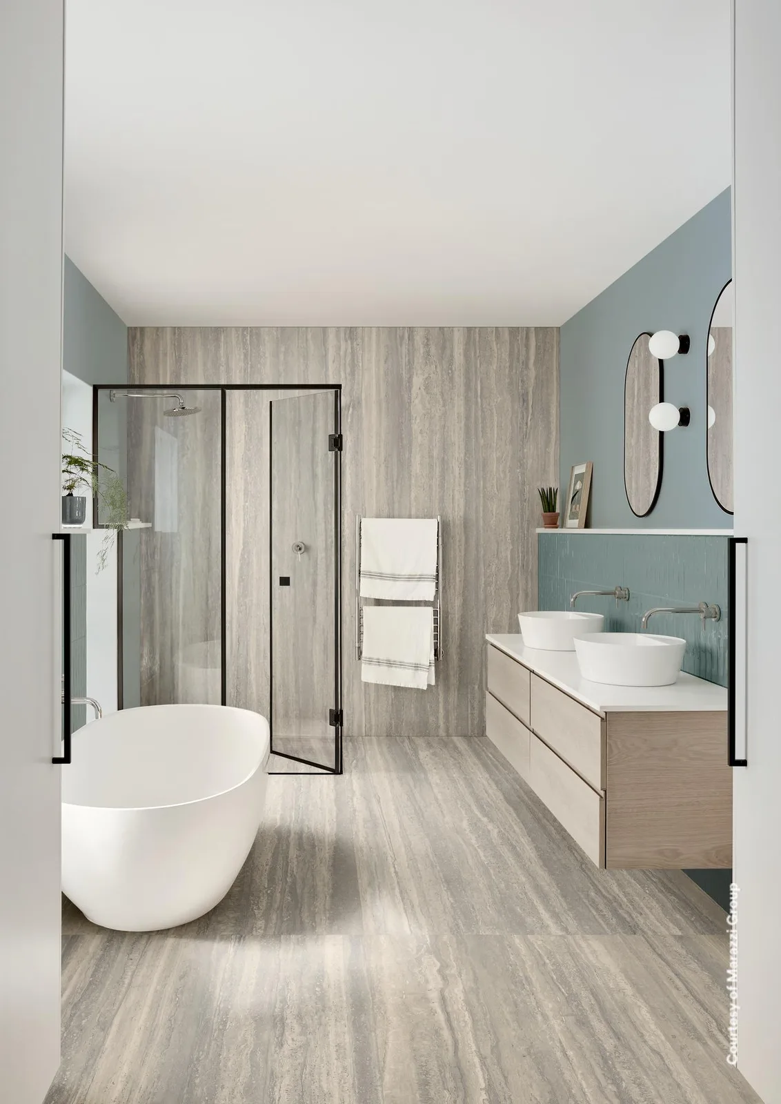 Bad mit Boden und Wand in grauer Travertin-Optik, freistehender Wanne, Doppelwaschtisch und Glasdusche.