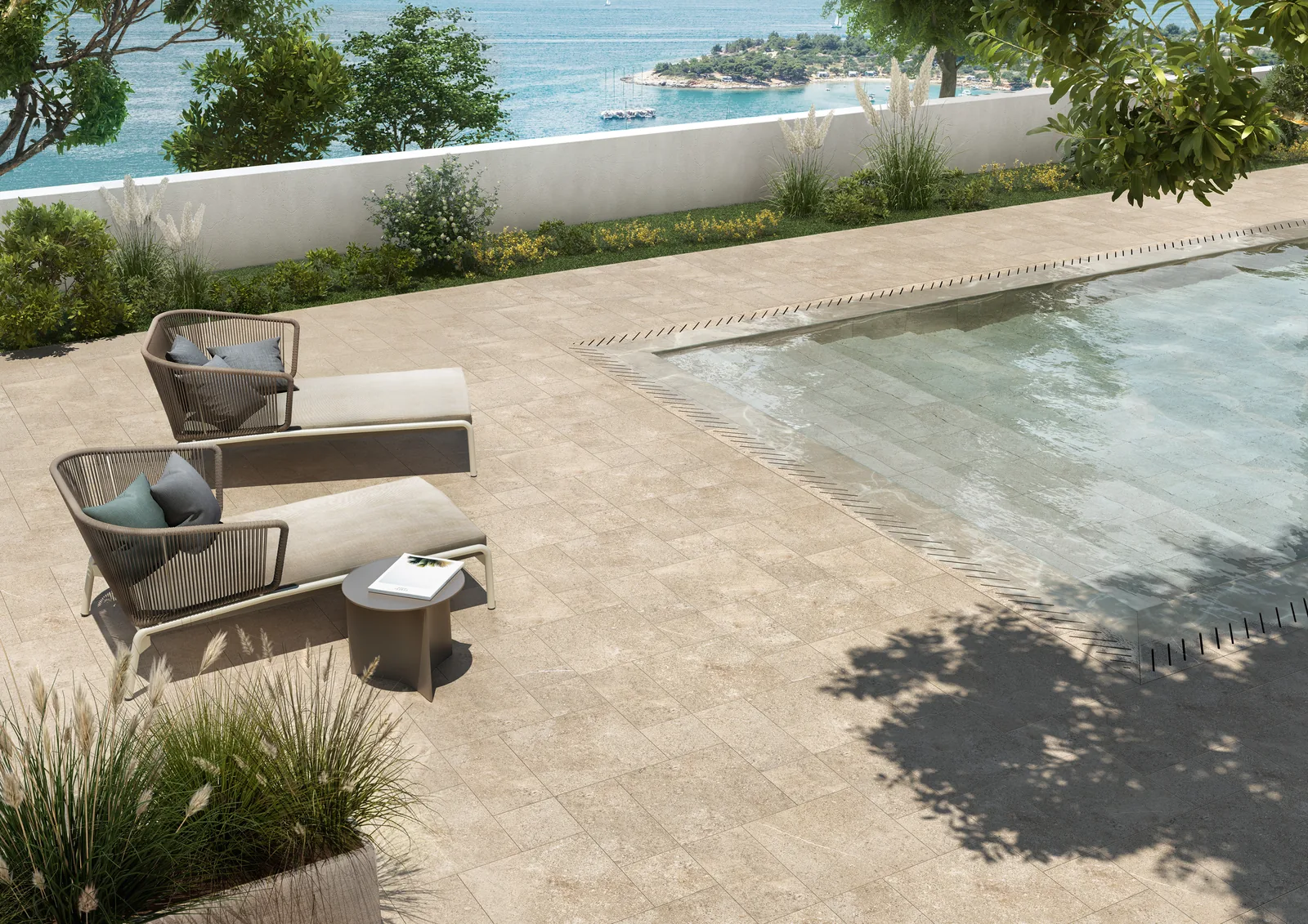 Poolterrasse mit sandbeigen Steinoptik-Fliesen in gemischten Formaten, Liegen, Gräsern und Meerblick.