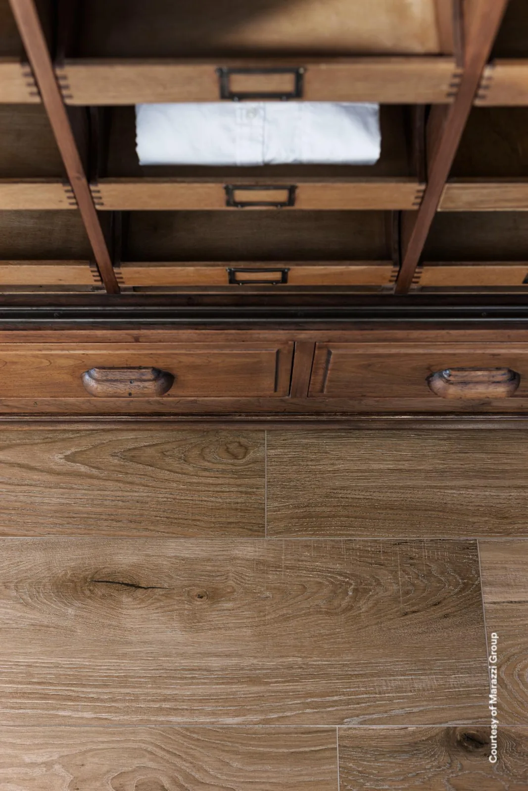 Warmbrauner Holzoptik-Boden in Dielen vor einem alten Holzschrank mit Schubladen und offenen Fächern.