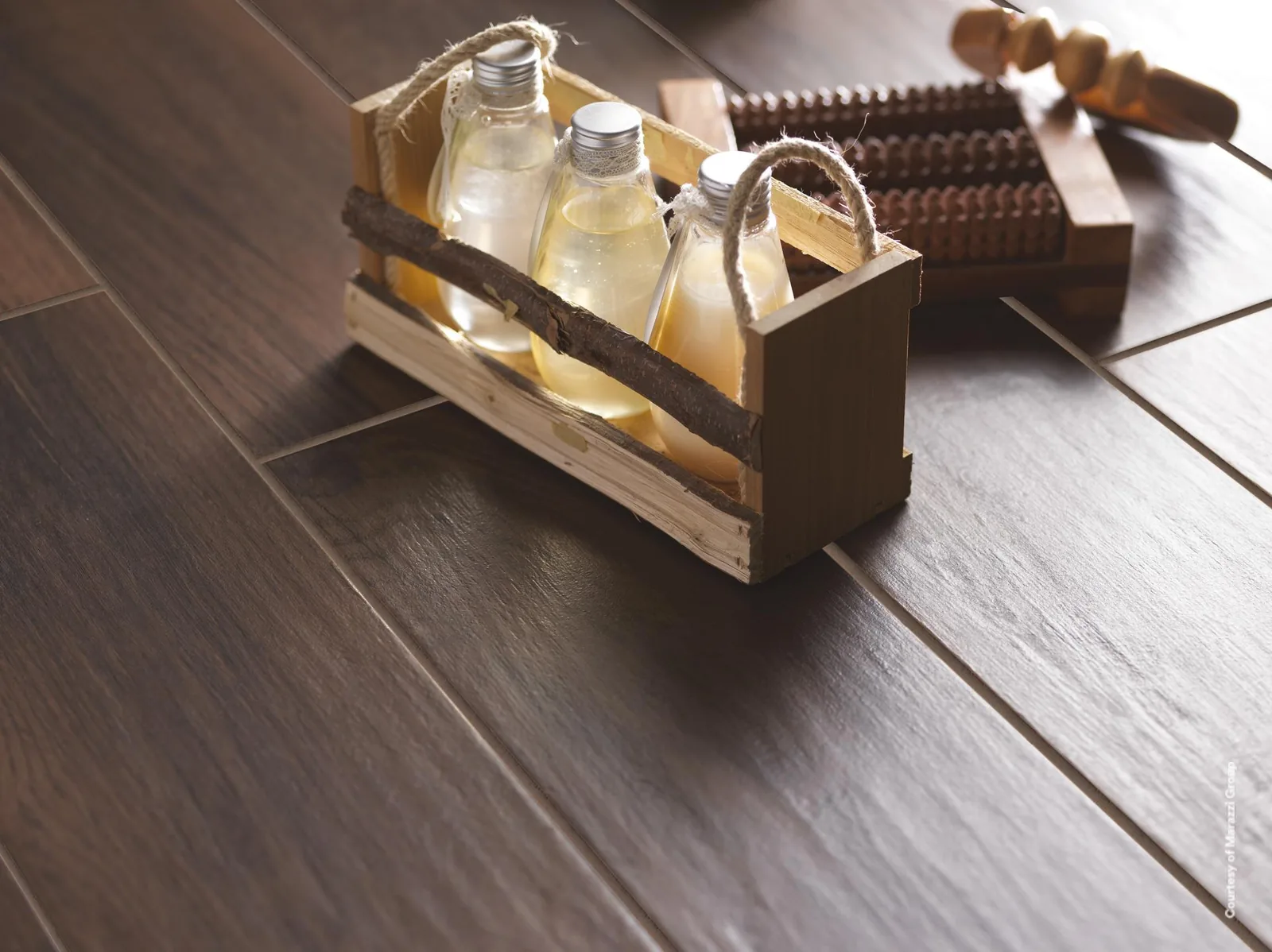 Holzkiste mit Glasflaschen und Massageroller auf dunkelbraunen Holzoptik-Dielen, Nahaufnahme der Fugen.