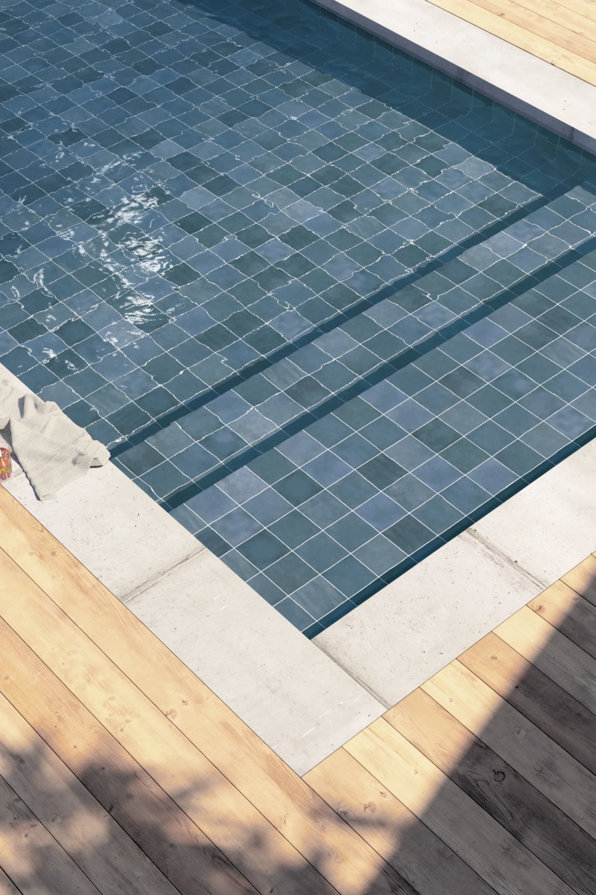Poolbecken mit dunkel-blaugrünen Fliesen, Treppenstufen und angrenzendem Holzdeck im Sonnenschein.