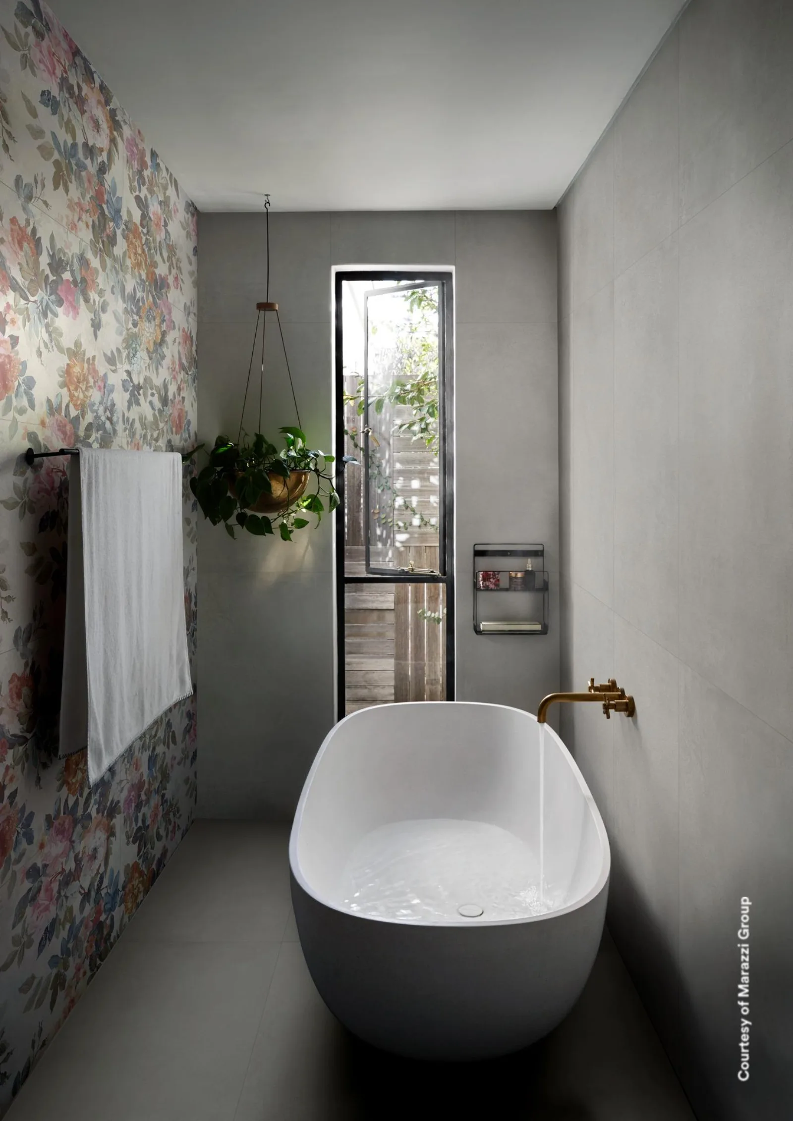 Schmales Bad mit freistehender Wanne, mittelgrauen Betonoptik-Wänden und einem Blumenpaneel an der linken Wand.