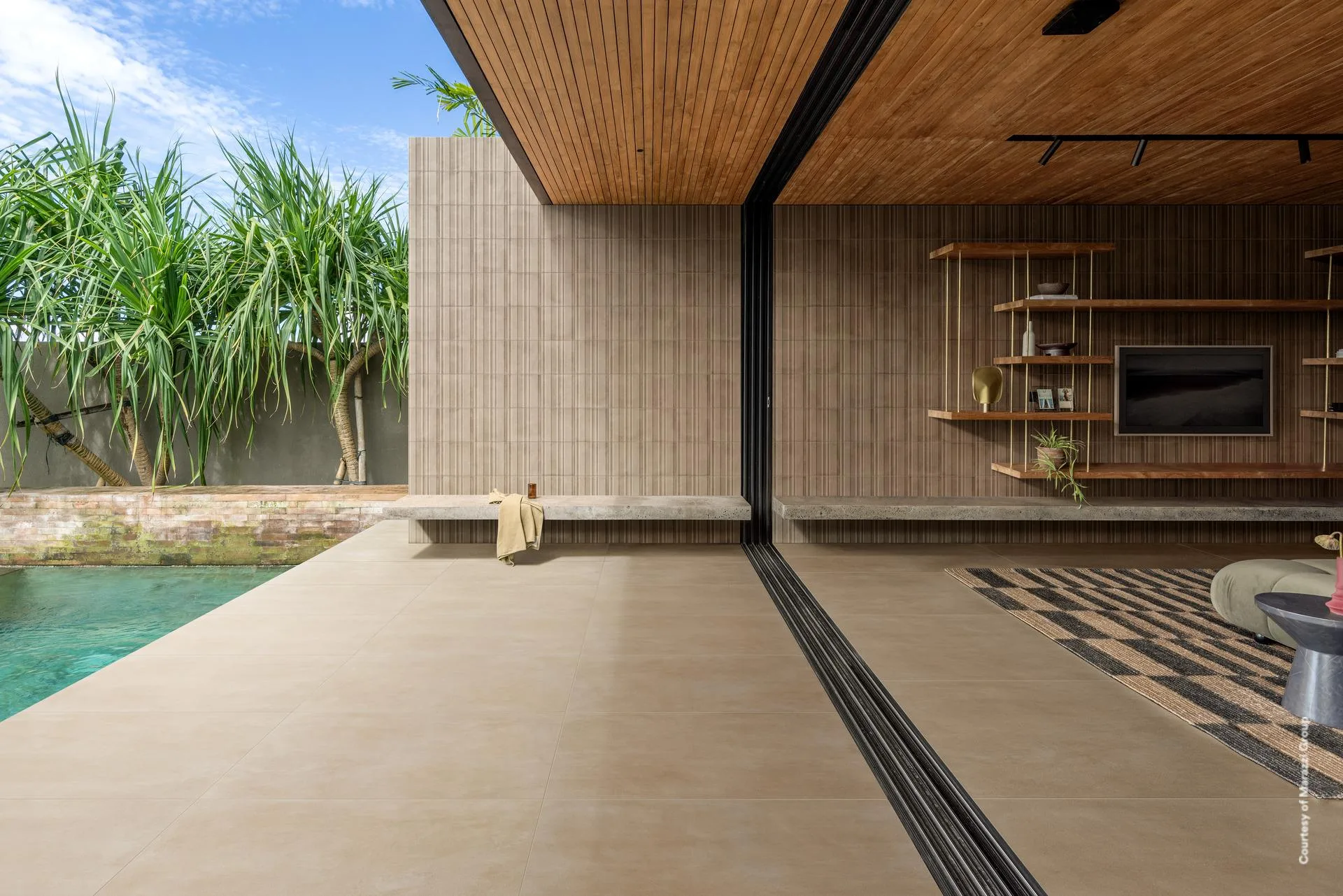 Poolterrasse mit sandfarbenen Großformatplatten in Betonoptik, die durch eine offene Glasfront in den Wohnraum weiterlaufen.