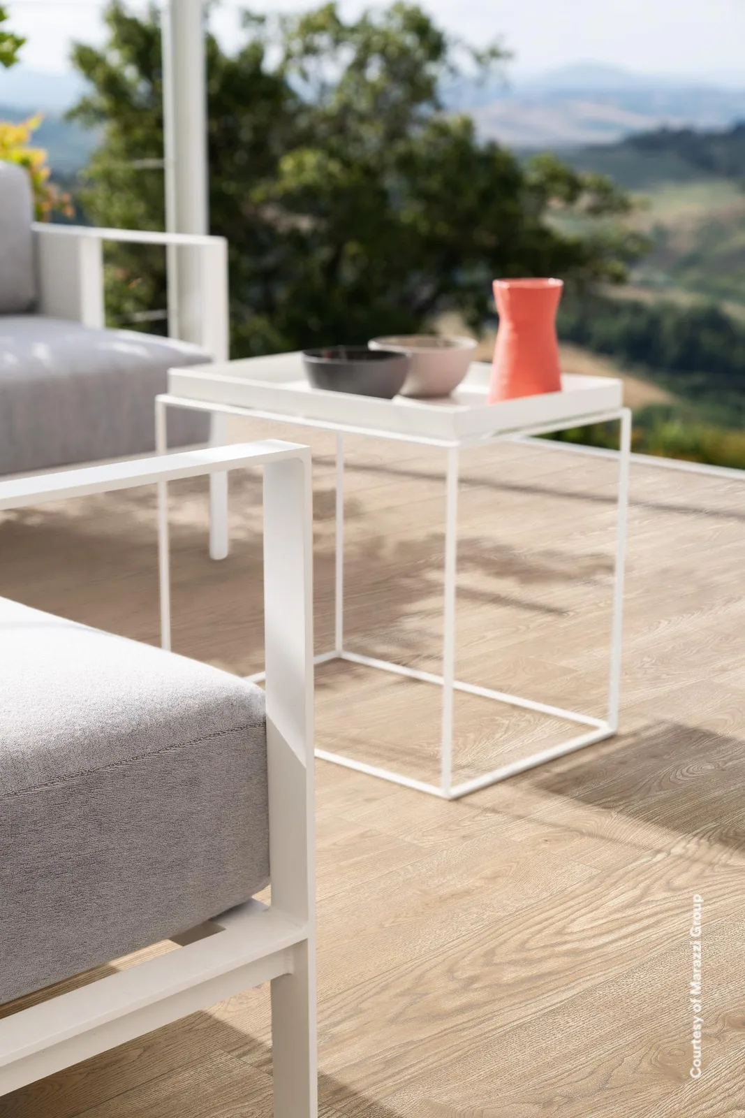 Terrasse mit Lounge-Sessel und Beistelltisch vor Hügellandschaft, Boden in hellbeigen Holzoptik-Planken.
