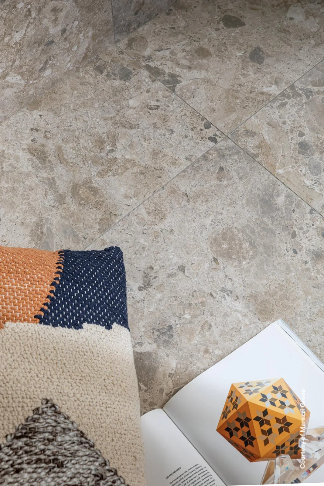 Nahaufnahme eines Bodens in heller Terrazzo-Optik mit großen Steinsplittern, darauf Kissen, Buch und Würfel.