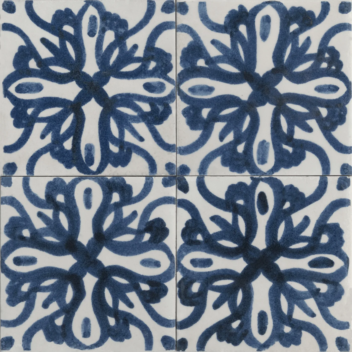 Vier glänzende Fliesen 15x15 cm mit großer blauer Blütenrosette aus geschwungenen Ranken auf weißem Grund.