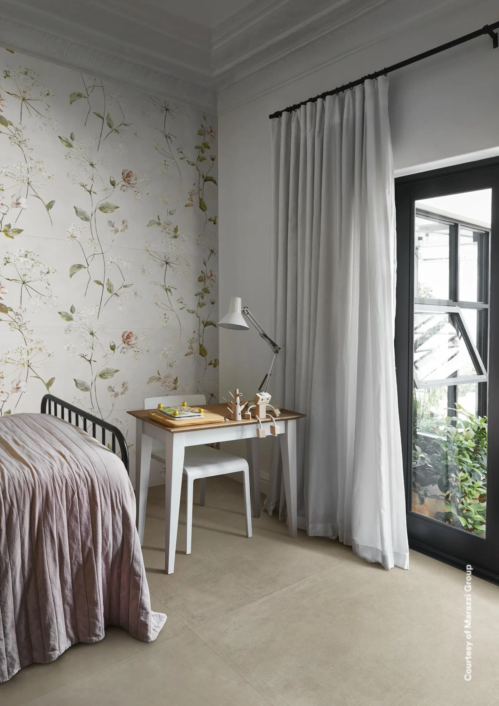 Schlafzimmer mit Bett, kleinem Schreibtisch und Vorhang am Fenster auf beigegrauem Betonoptik-Boden im Großformat.