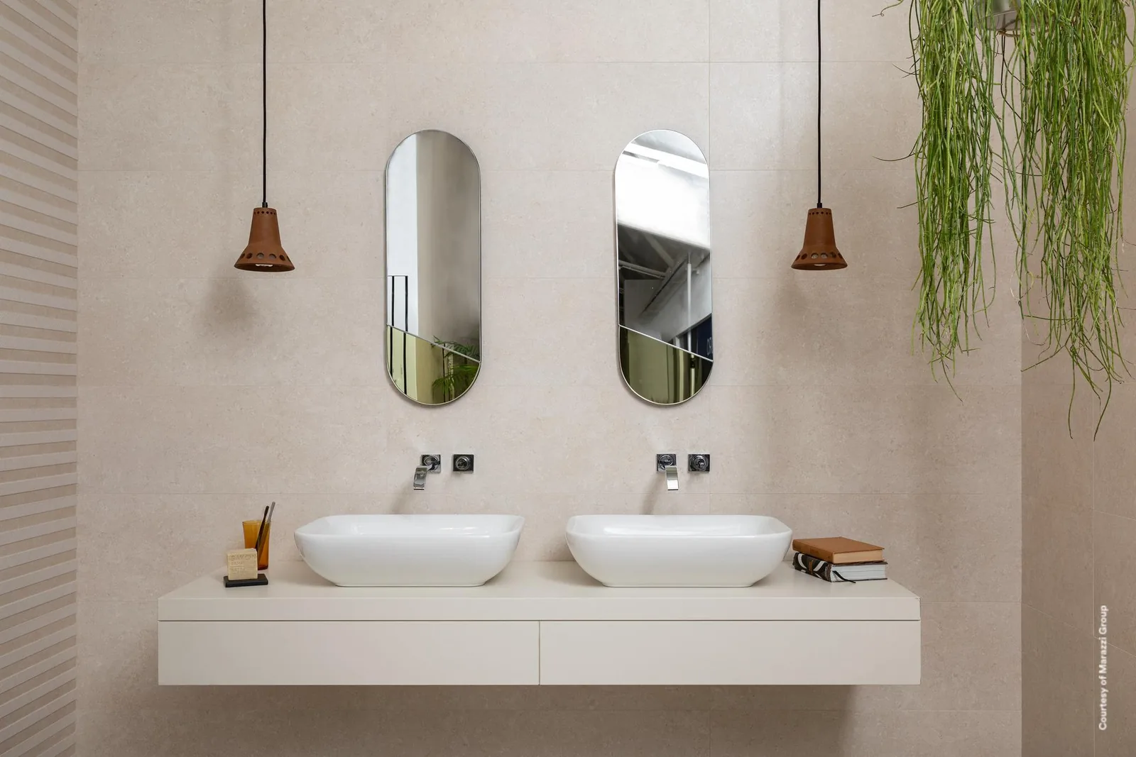 Bad mit zwei Aufsatzwaschbecken und ovalen Spiegeln, Wände in hellbeiger Steinoptik, links mit Reliefstreifen.