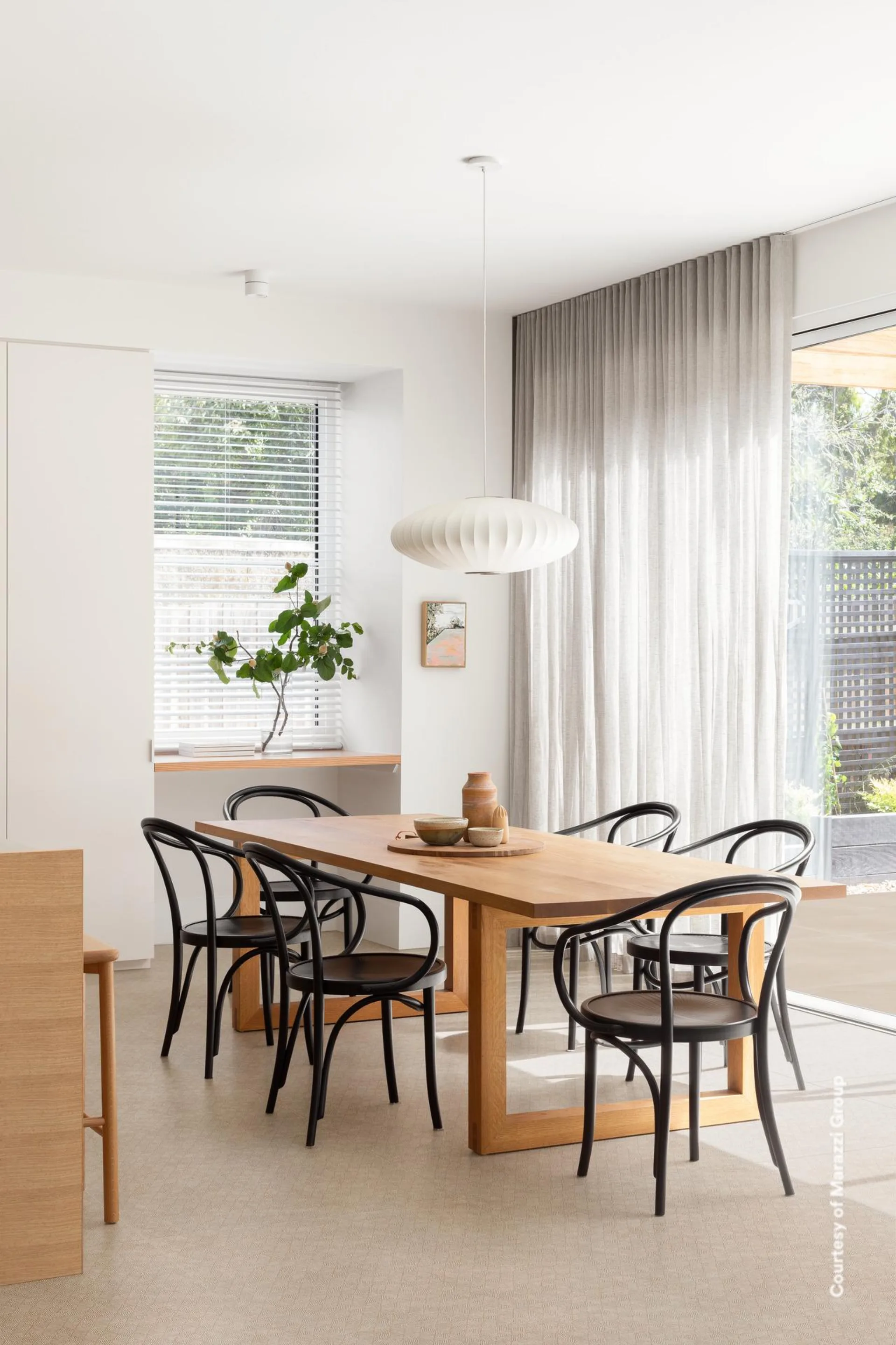 Essbereich mit Holztisch, schwarzen Bugholzstühlen und Fensterfront auf hellbeigem Betonoptik-Boden.