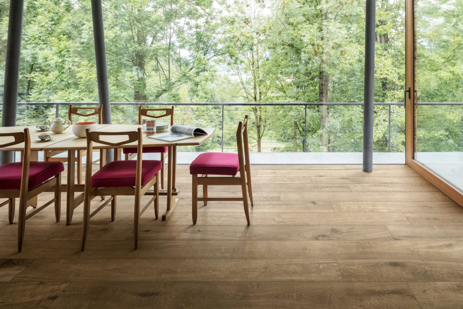 Essbereich mit Holztisch und roten Stühlen auf Dielenboden in heller Honig-Eichenoptik, Glasfront mit Blick ins Grüne.