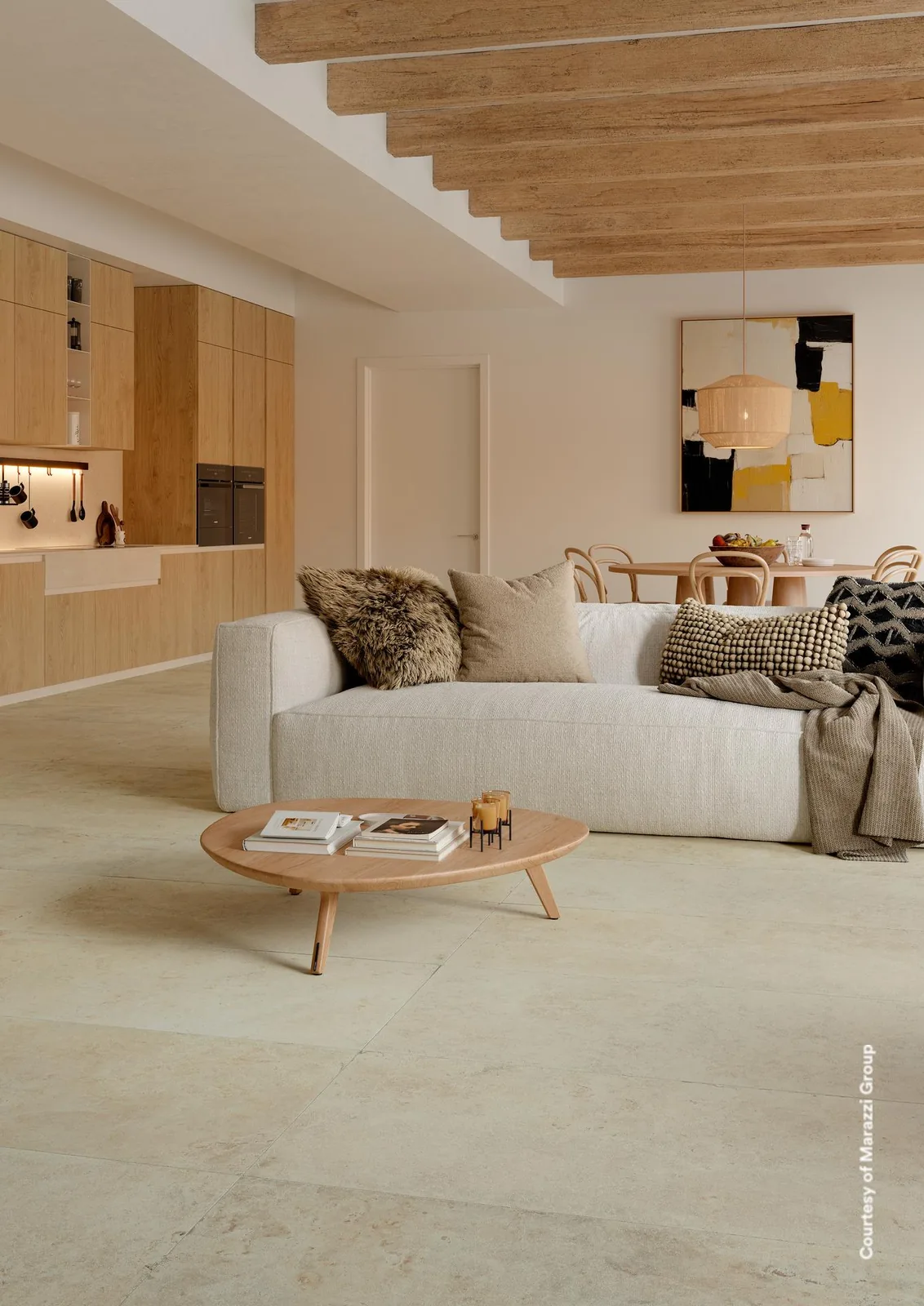 Offener Wohnraum mit Küche, cremefarbene Steinoptik-Bodenfliesen im Großformat, helles Sofa und runder Couchtisch