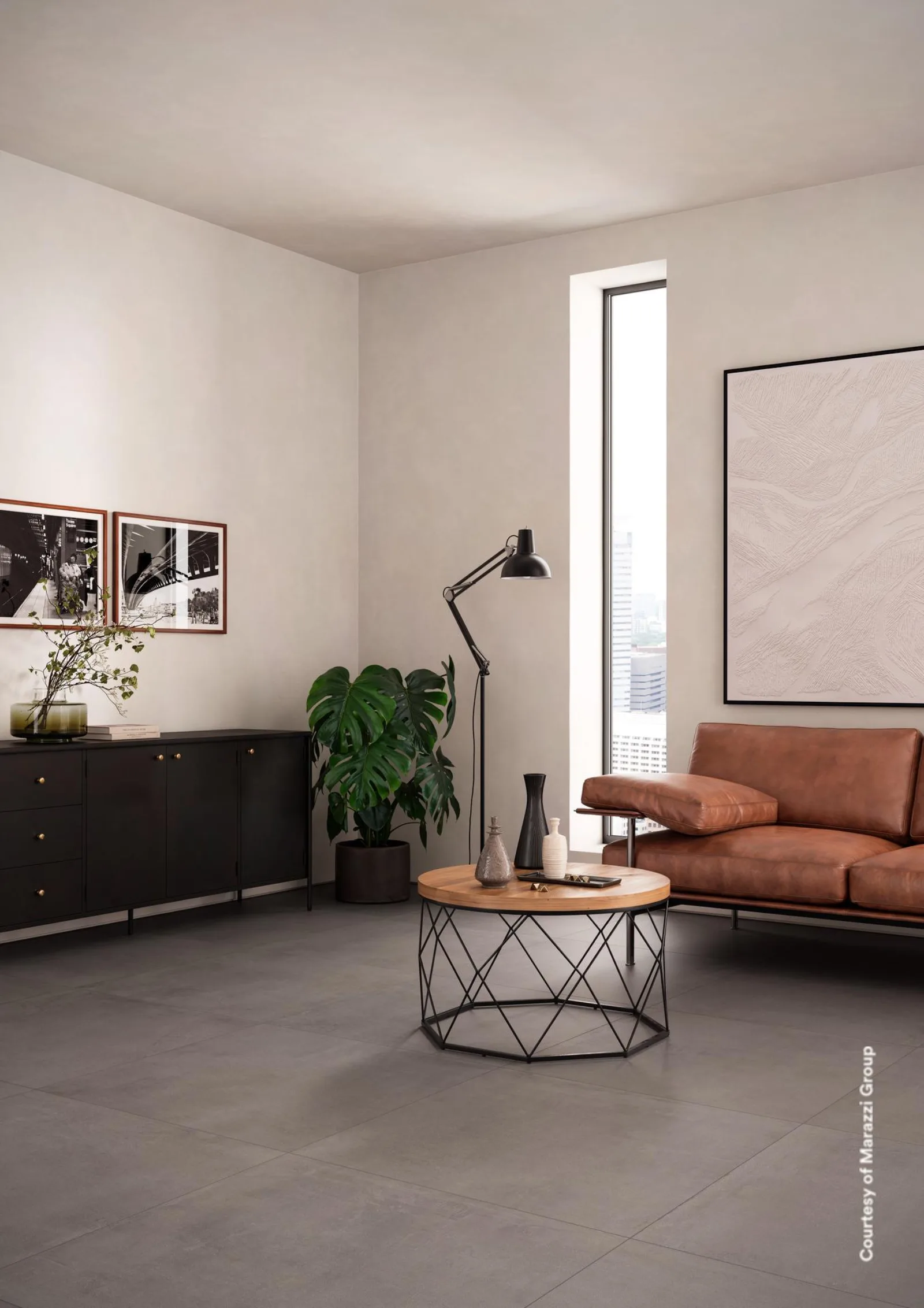 Wohnzimmer mit Ledersofa, rundem Beistelltisch und schwarzem Sideboard auf dunkelgrauem Betonoptik-Boden.